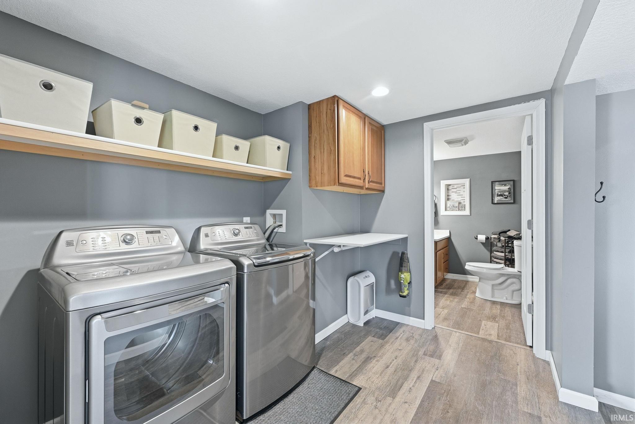 Dedicated laundry area featuring a front-load washer and top-load dryer, wood-finish flooring, and light gray wall paint