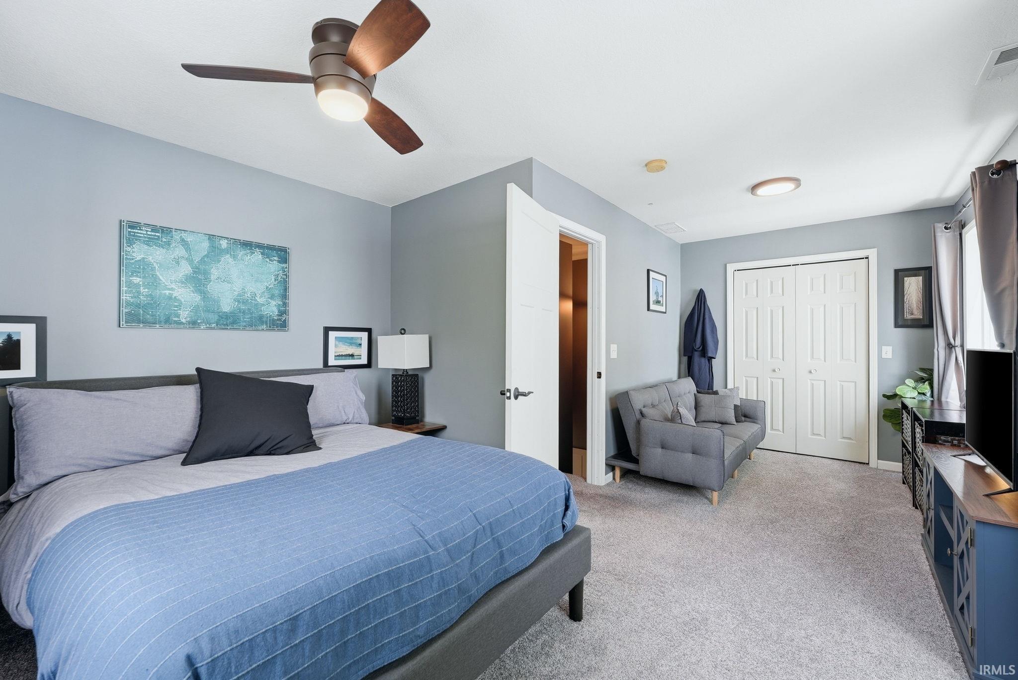 Spacious bedroom featuring light gray walls, plush carpeting, a modern ceiling fan with integrated lighting, a flush-mount ceiling light, and bi-fold closet doors