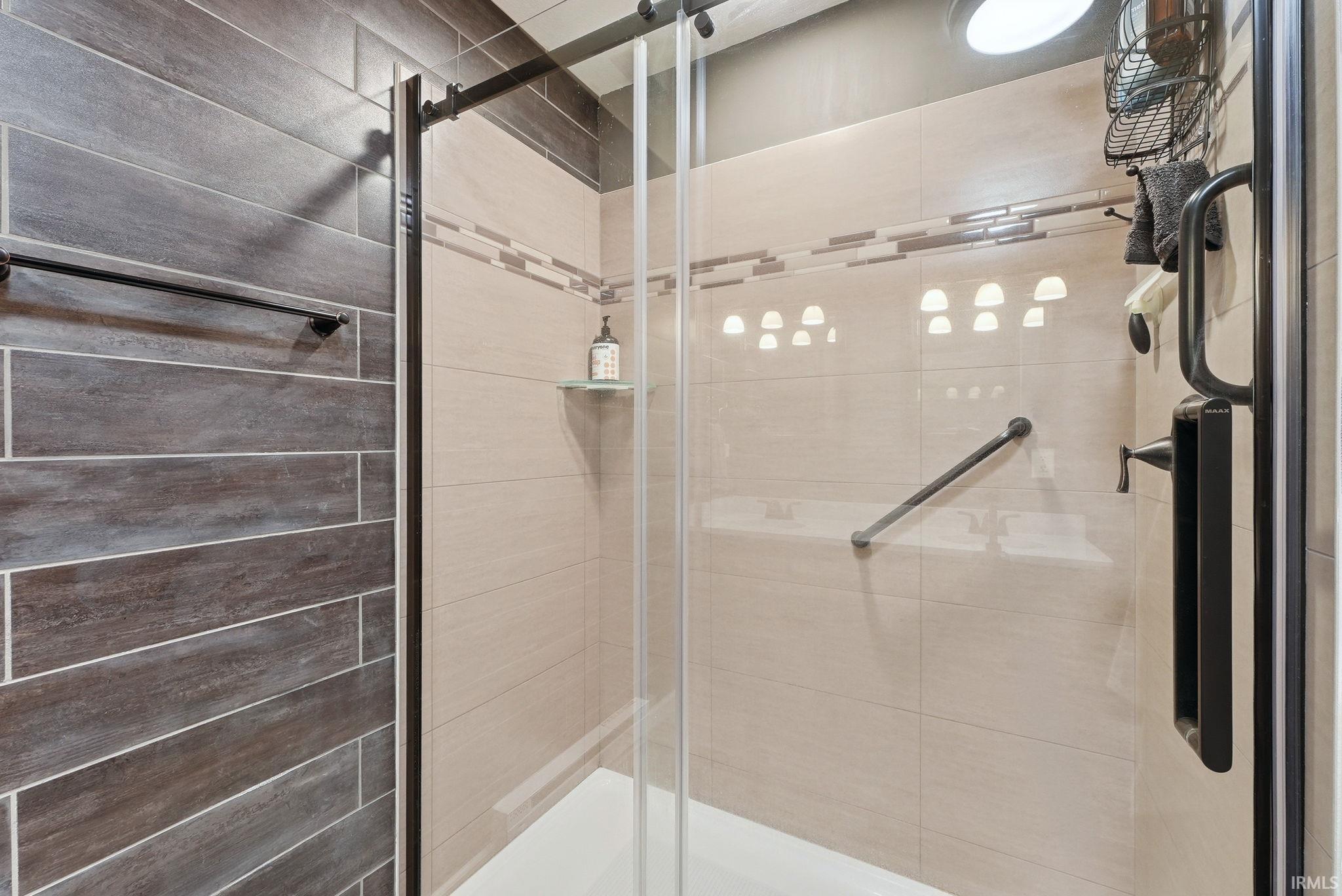 Shower enclosure with clear glass door, showcasing plank-style wall tiling and lighter rectangular wall tiles with a decorative band