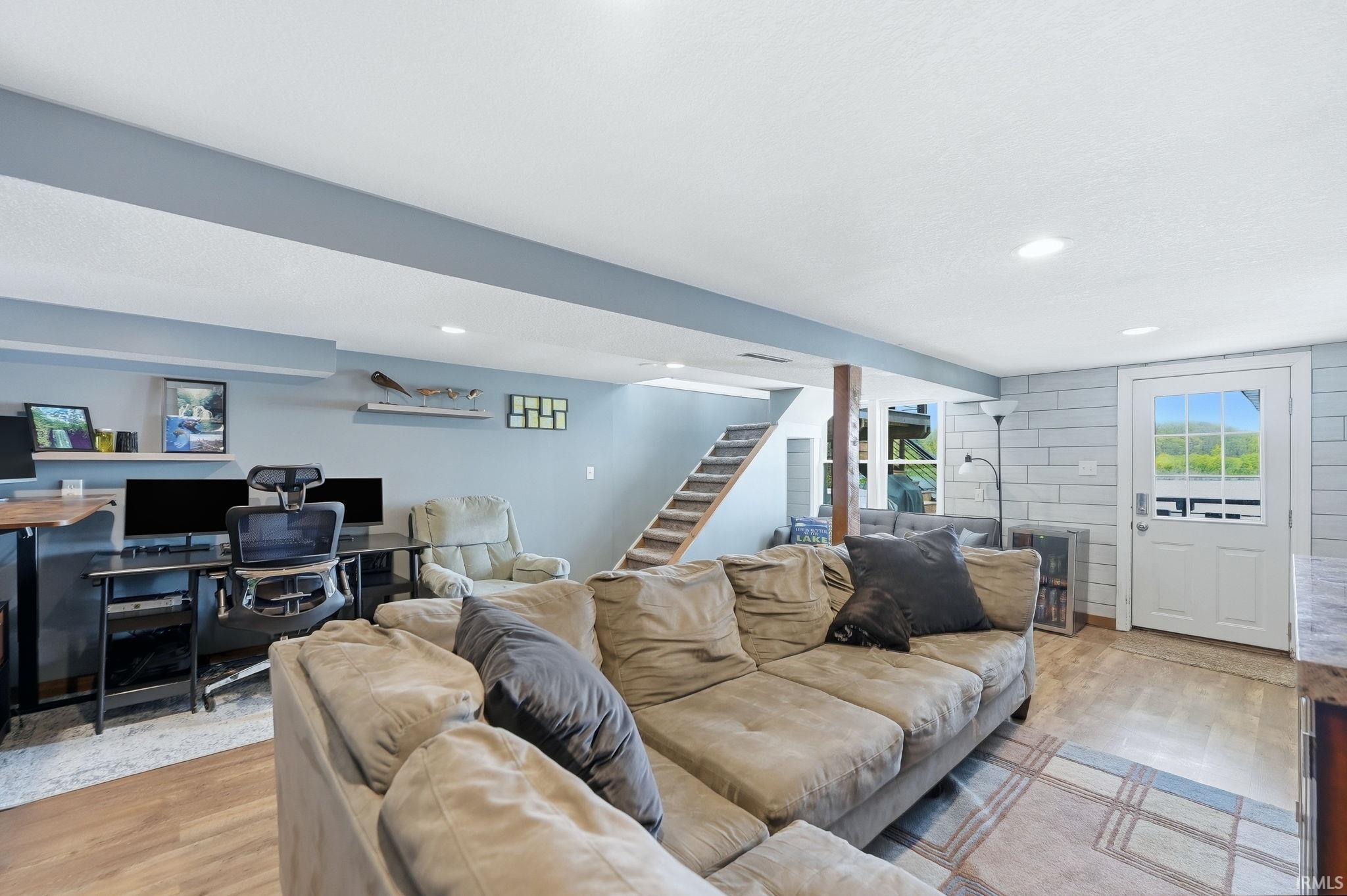 Finished recreation room featuring a staircase with wood treads, light wood-finish flooring, recessed lighting, and a white paneled door with a multi-pane window
