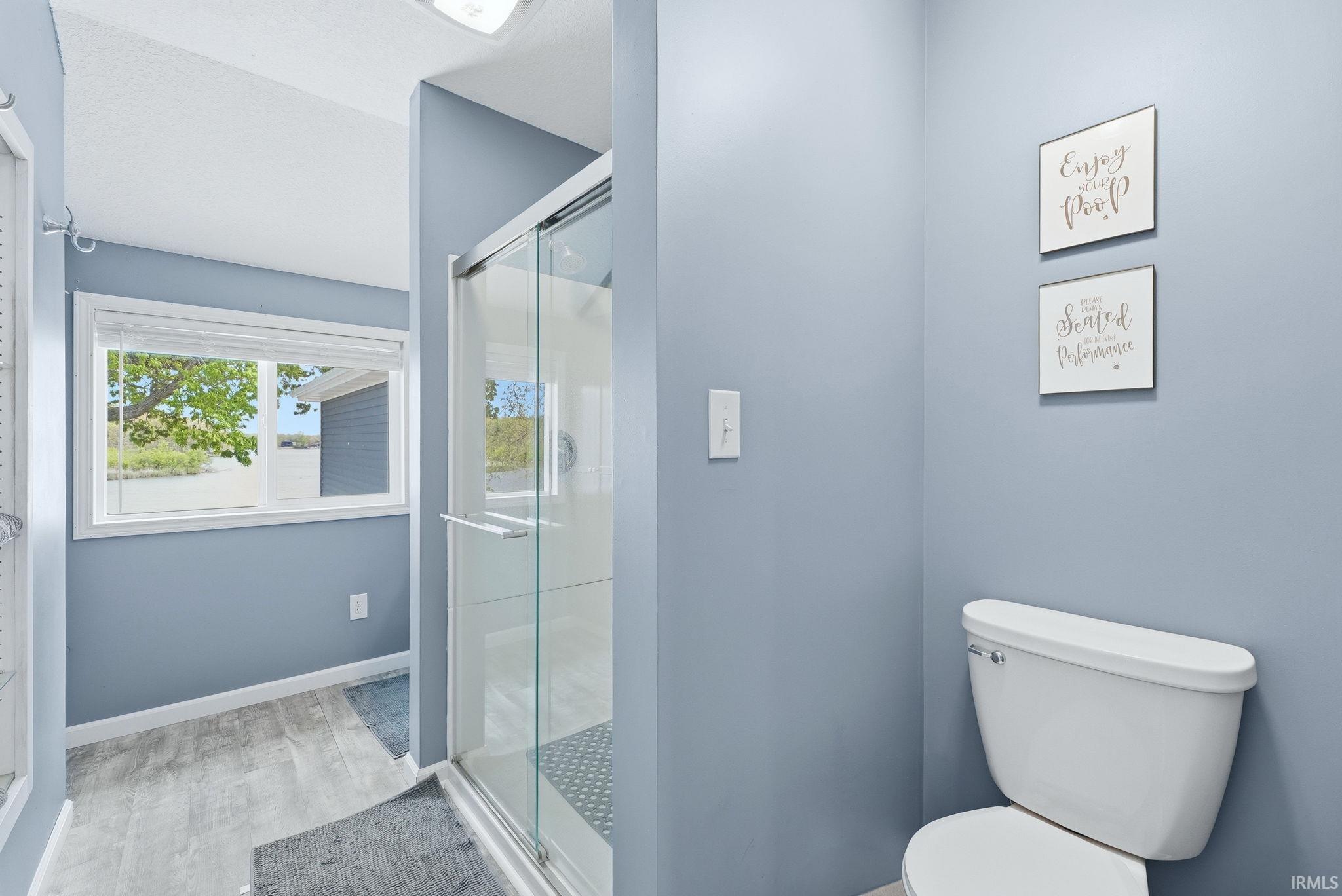 Bathroom featuring a white toilet, glass-enclosed shower, and a window with exterior visibility