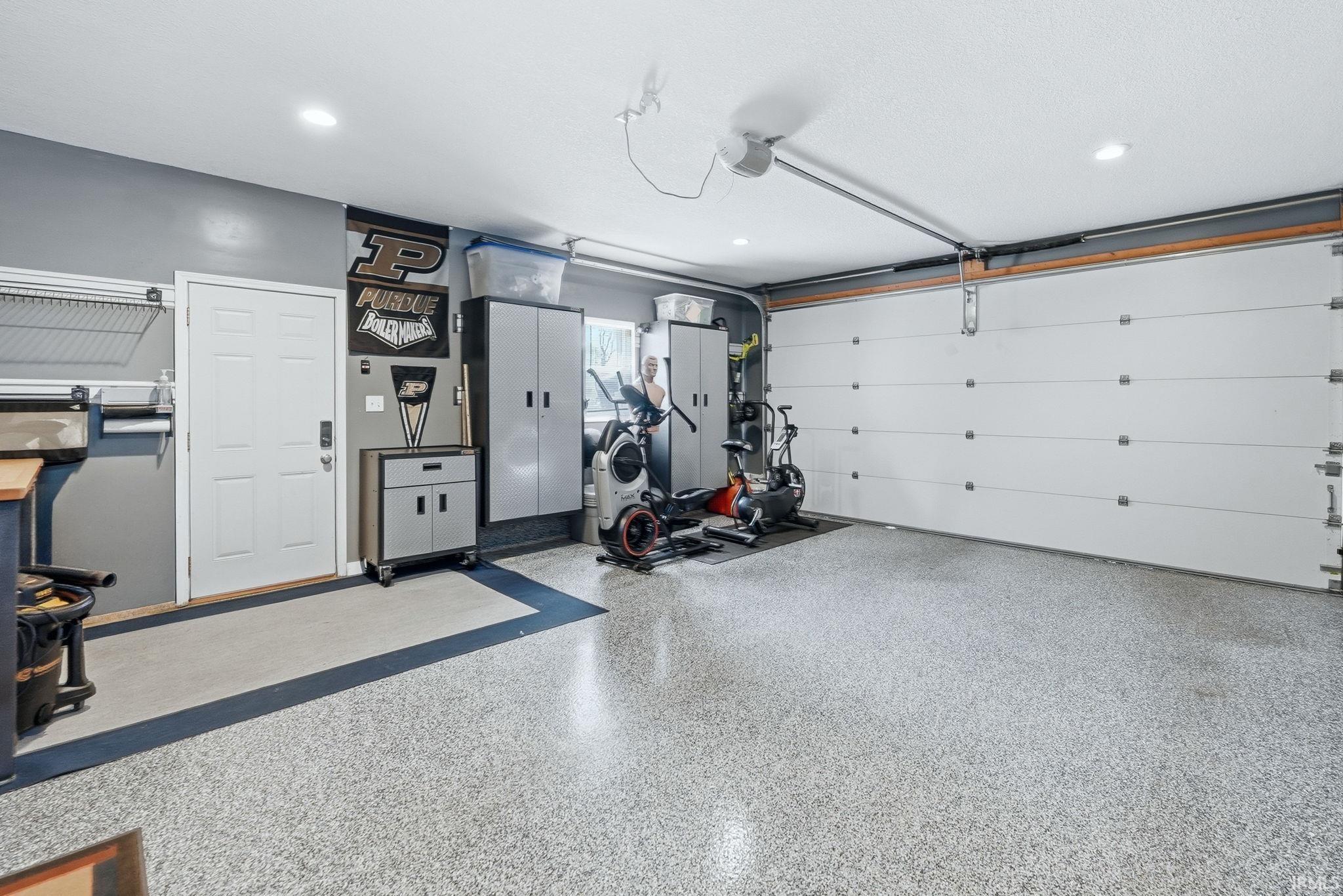 Spacious garage with an epoxy floor finish, overhead lighting, a white panel garage door, a side entry door, and built-in storage cabinets