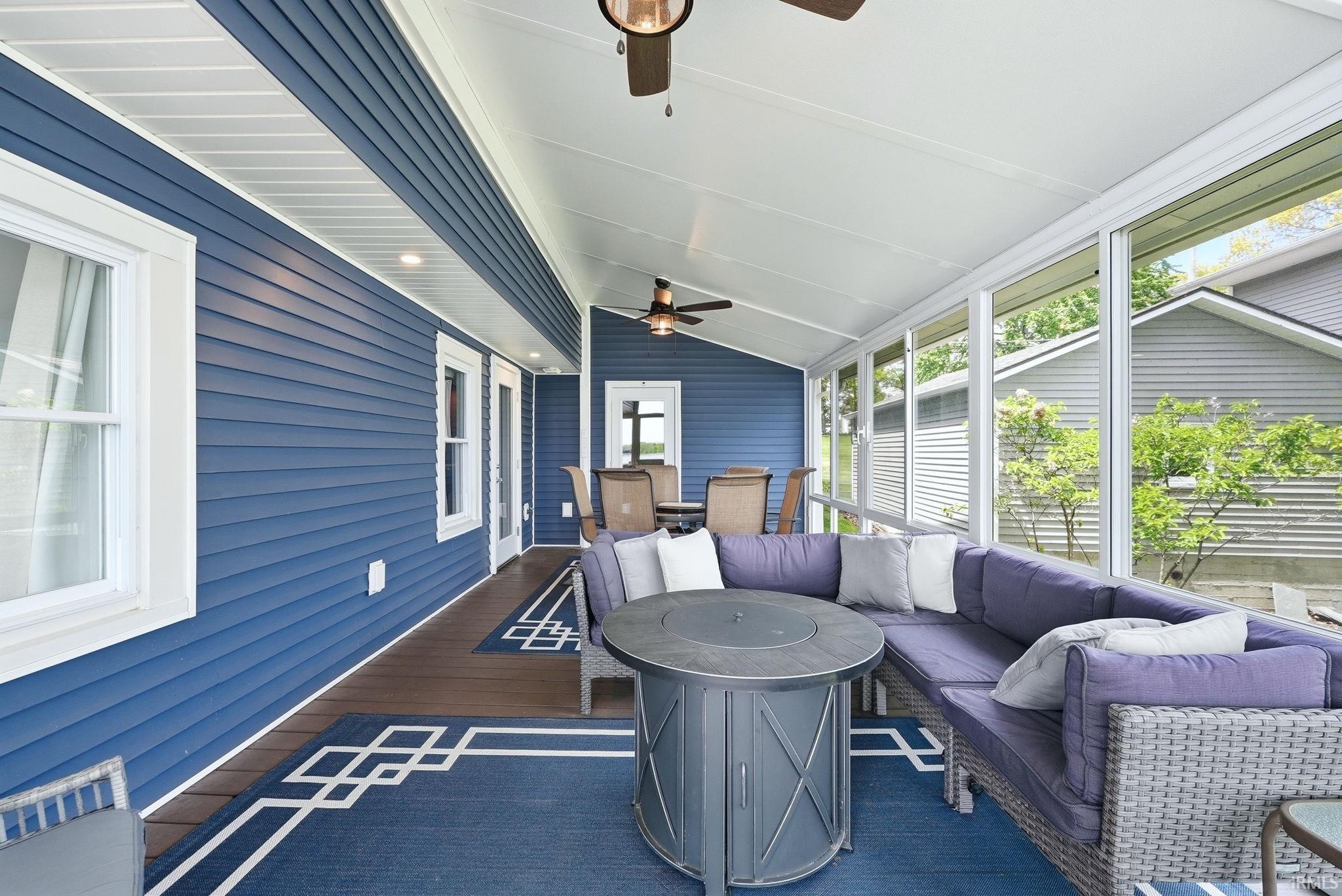 Screened porch featuring a vaulted ceiling with two ceiling fans, wood-finish flooring, and a blue exterior wall with white trim