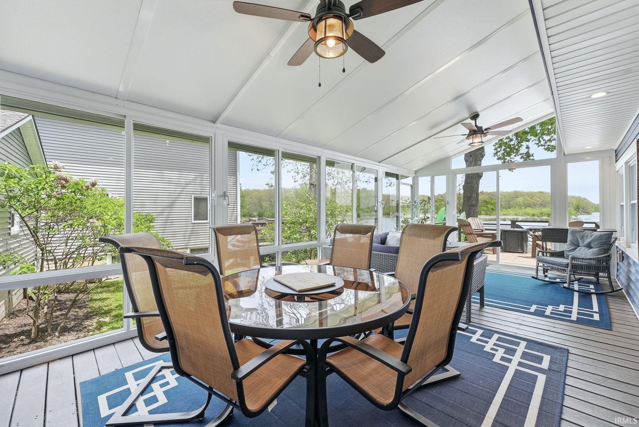 Spacious enclosed porch featuring a vaulted ceiling with two ceiling fans, white wood-finish flooring, and expansive windows overlooking the water