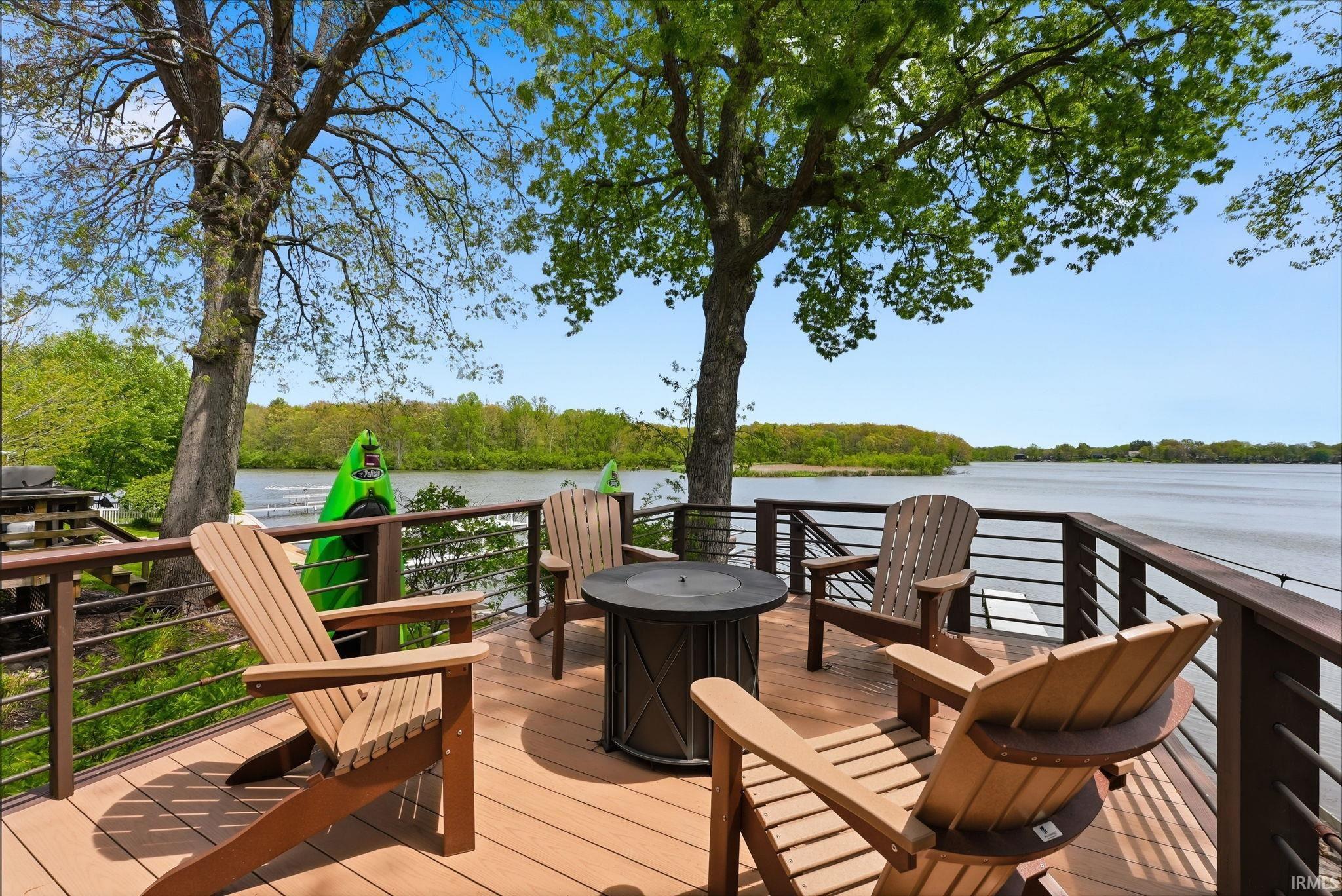 Spacious waterfront deck featuring composite decking, dark wood railings with cable infill, and mature trees providing natural shade