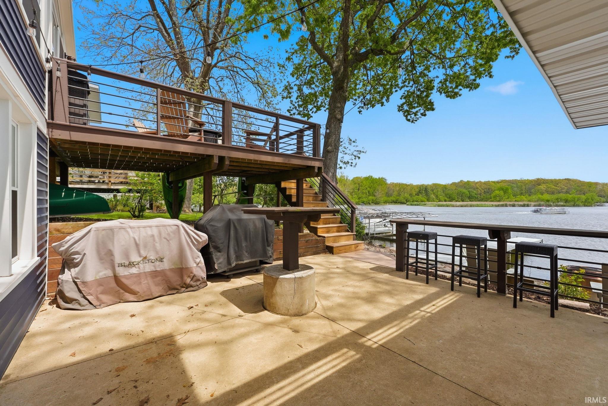 Waterfront concrete patio featuring a built-in bar with seating, a multi-level wooden deck with cable railings, and exterior siding