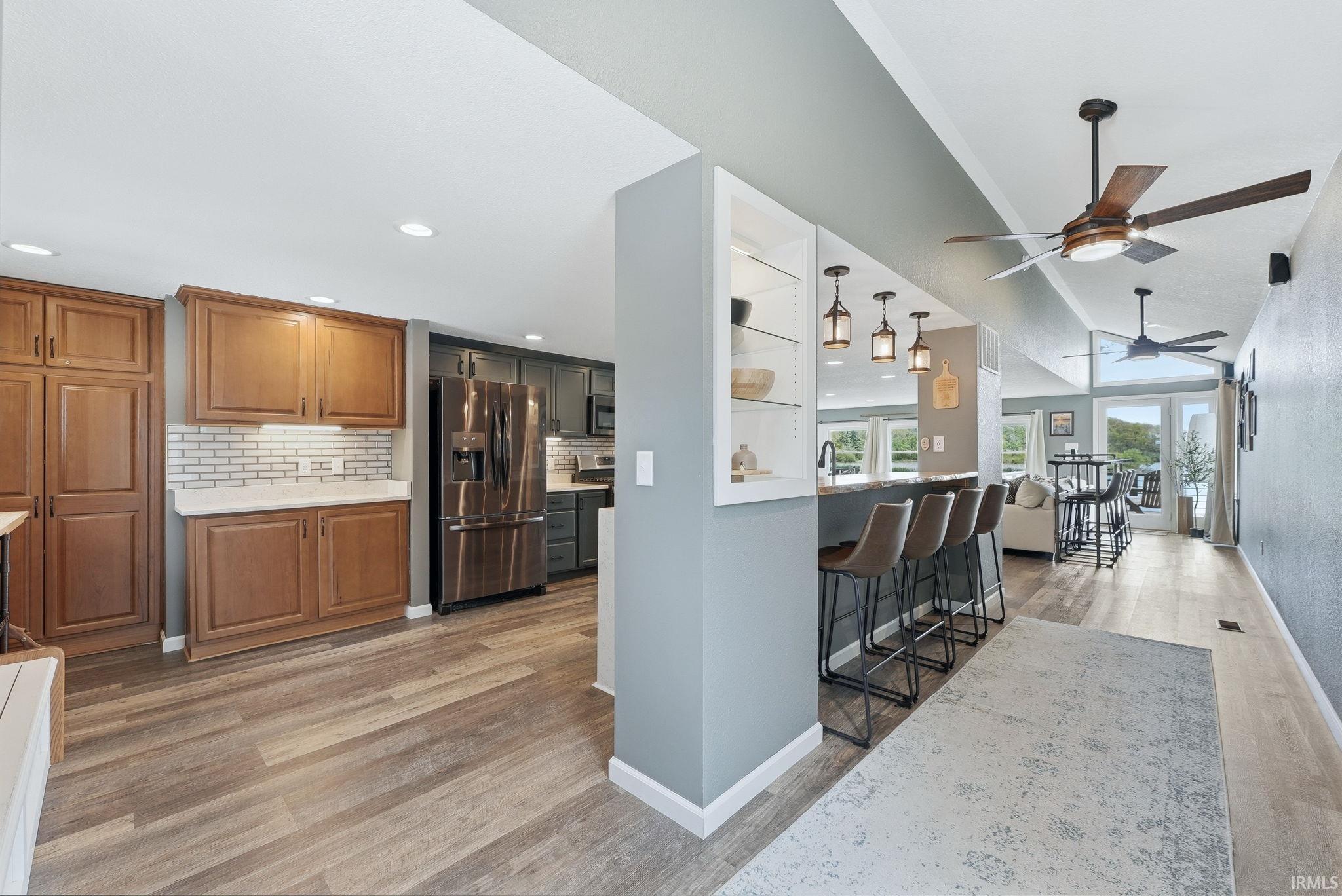 Open-concept interior featuring wood-finish flooring, a kitchen island with pendant lighting, vaulted ceilings, and ceiling fans