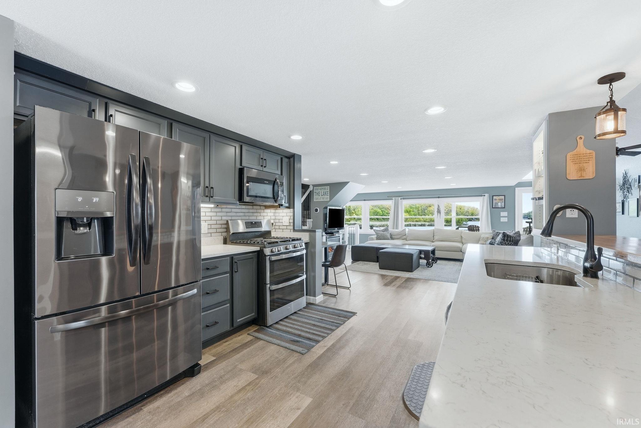 Modern kitchen featuring stainless steel appliances, dark gray cabinetry, light-toned countertops, and subway tile backsplash