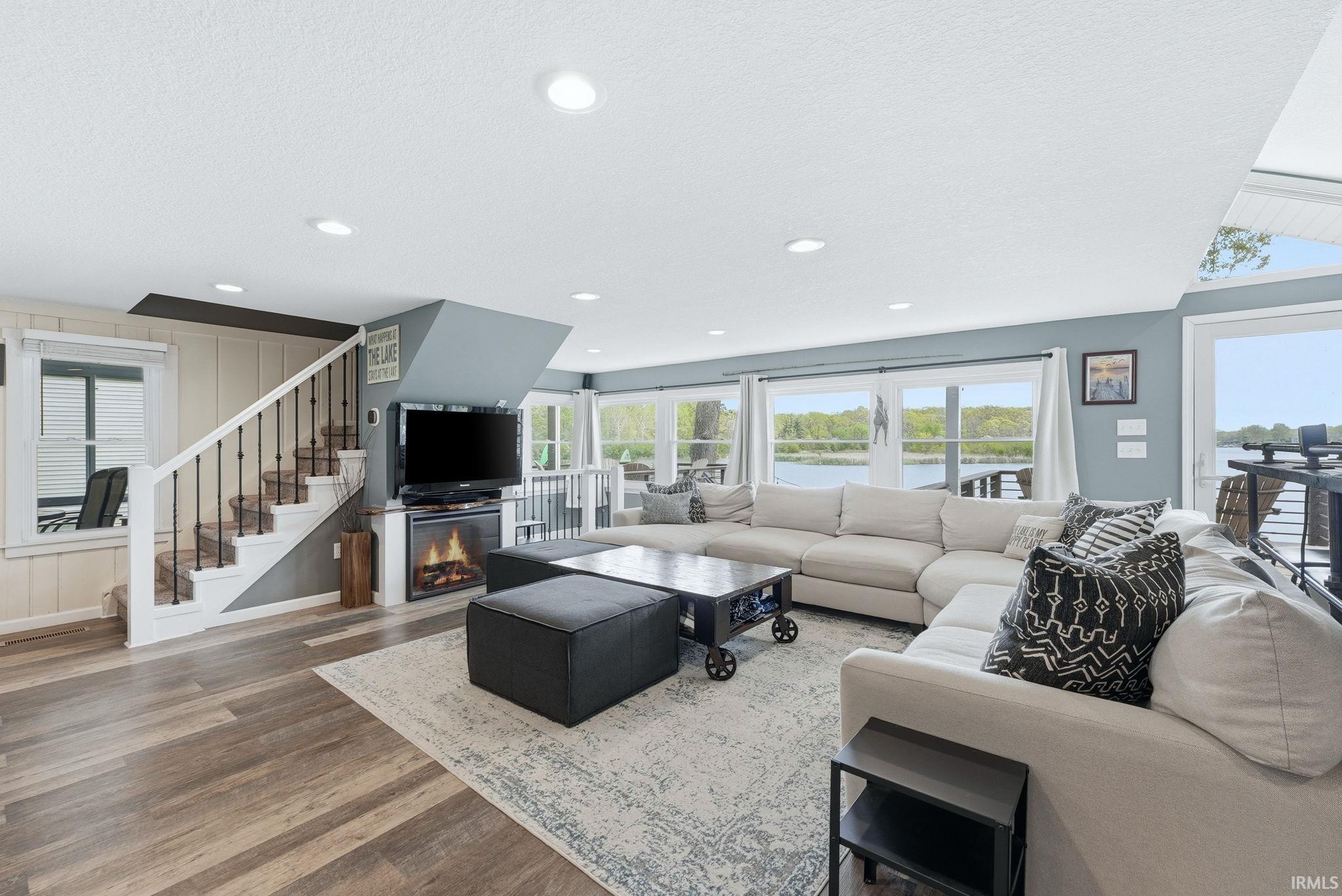 Living area featuring wood-finish flooring, recessed lighting, an electric fireplace, and a full wall of windows overlooking a body of water