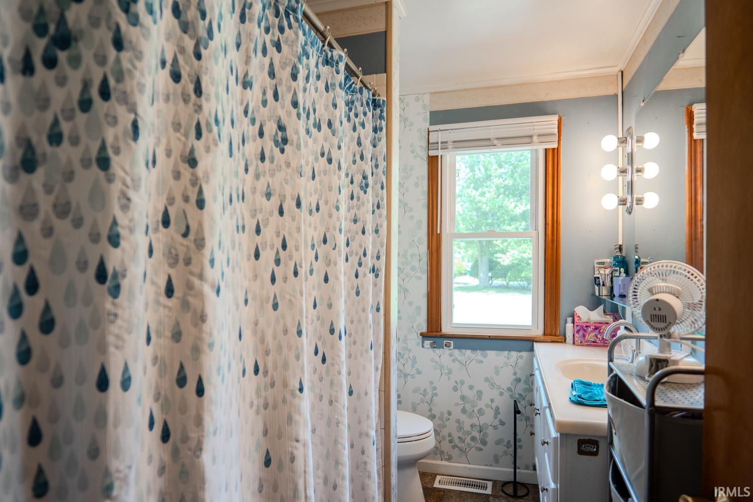 Bathroom featuring a vanity with an integrated sink, a window with wood trim, wall-mounted lighting, and a toilet