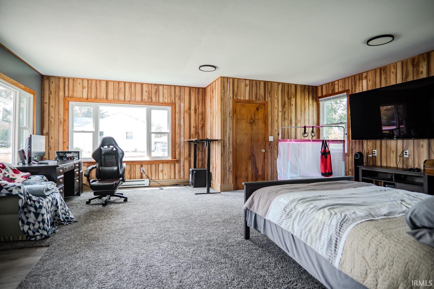 Spacious room featuring wood paneling, light-colored carpeting, two windows providing natural illumination, and a ceiling-mounted light fixture