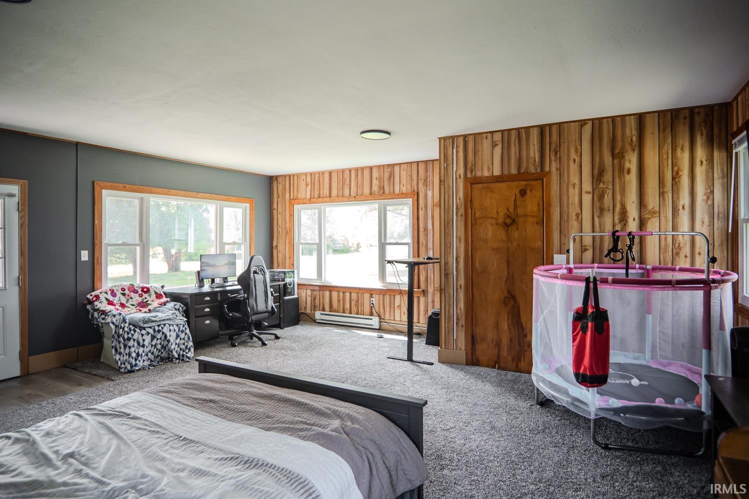 Spacious room featuring wood plank accent walls, multiple windows providing natural light, and plush grey carpeting