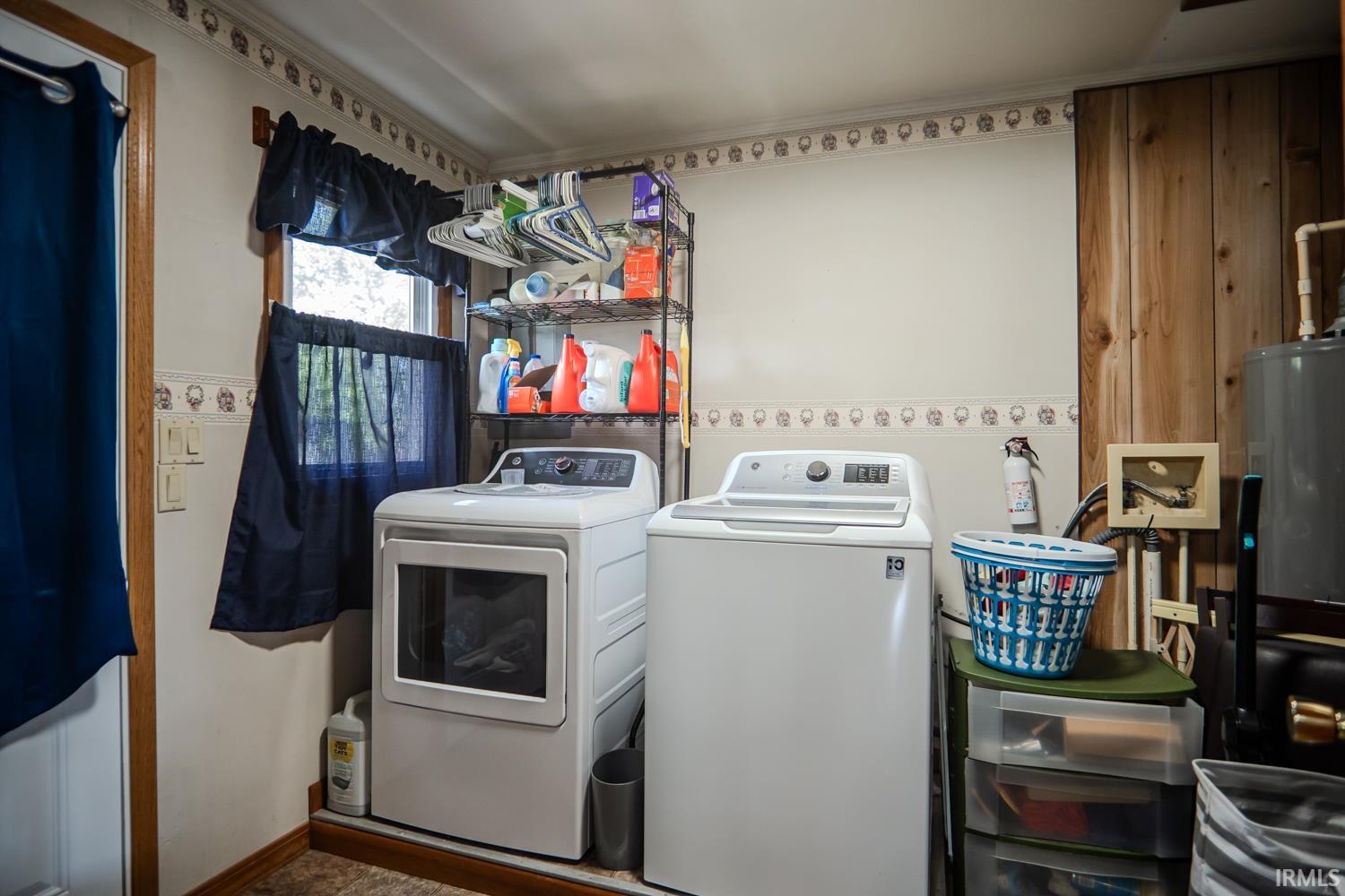 Dedicated laundry area featuring a window, built-in shelving, wood-finish flooring, and a water heater