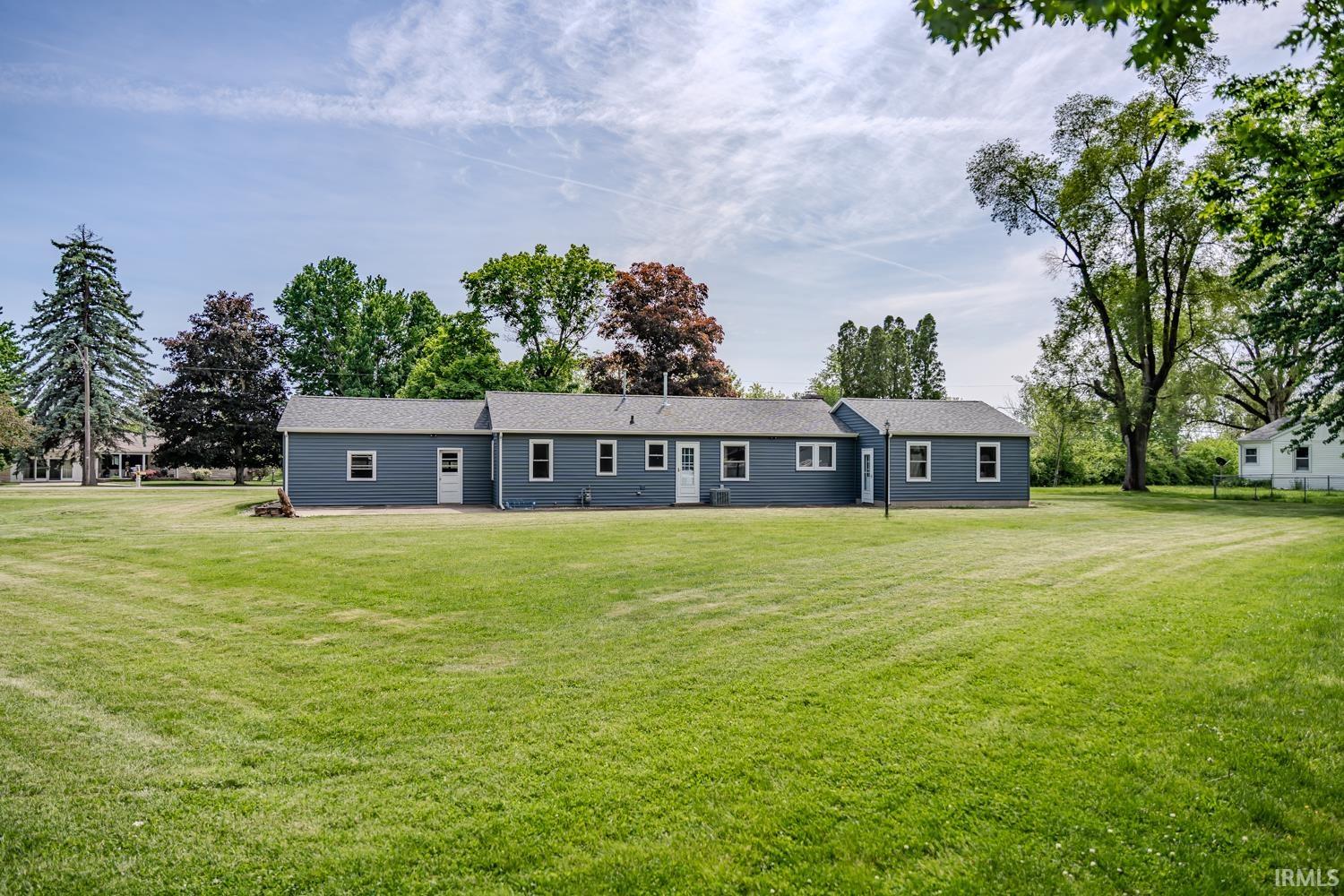 Expansive grassy yard featuring a gray-sided residence with white trim windows and multiple entry doors