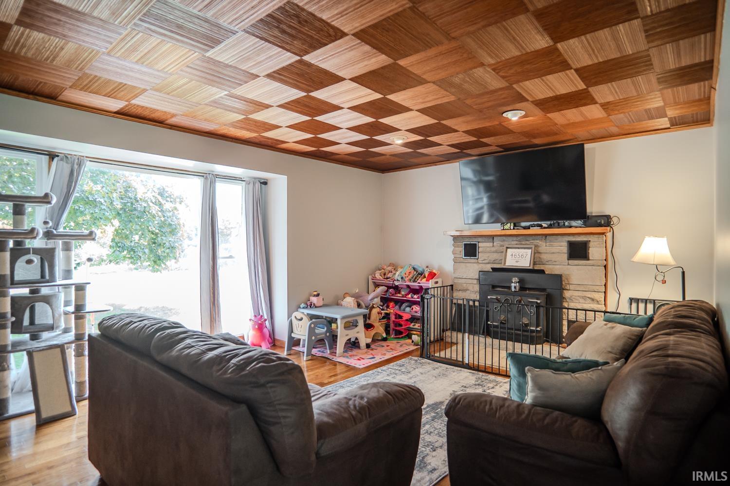 Living room featuring a checkerboard wood ceiling, stone-surround fireplace with a hearth, and large picture windows