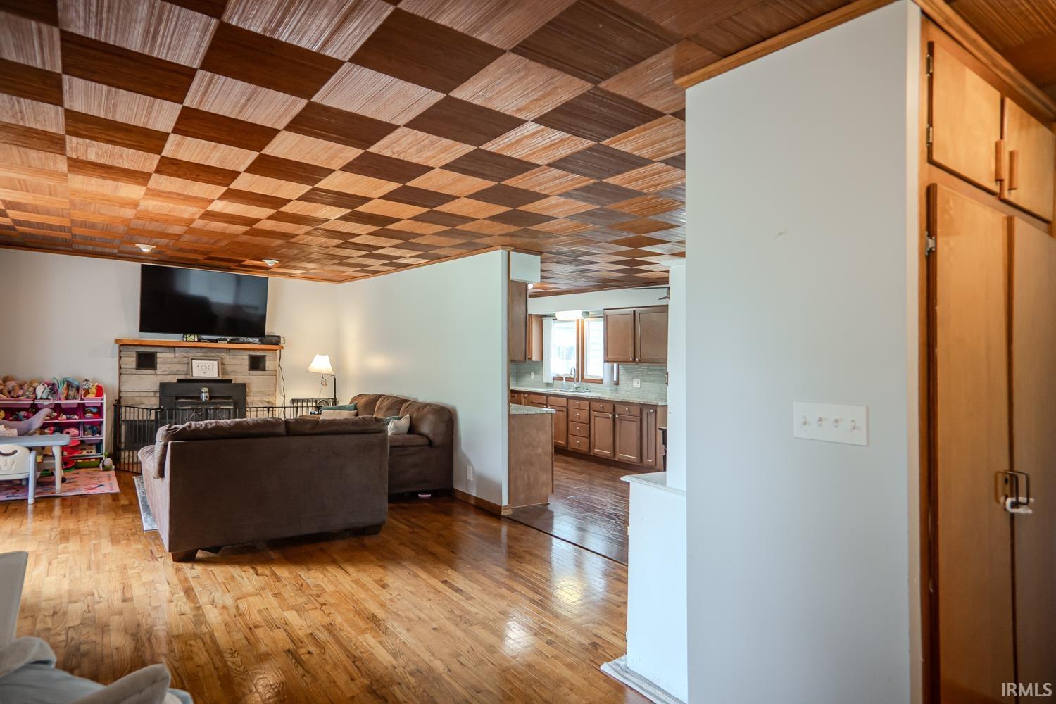 Living area featuring checkerboard wood-finish ceiling, hardwood flooring, and a stone-clad fireplace