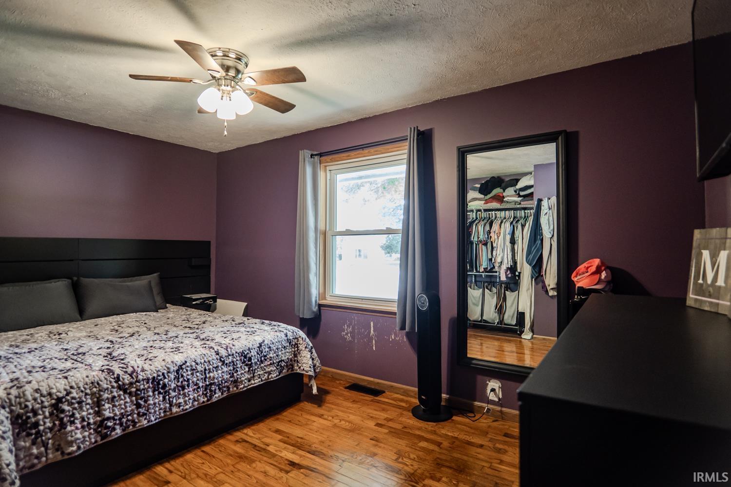 Bedroom featuring wood-finish flooring, a ceiling fan with integrated lighting, and a single window with wood trim