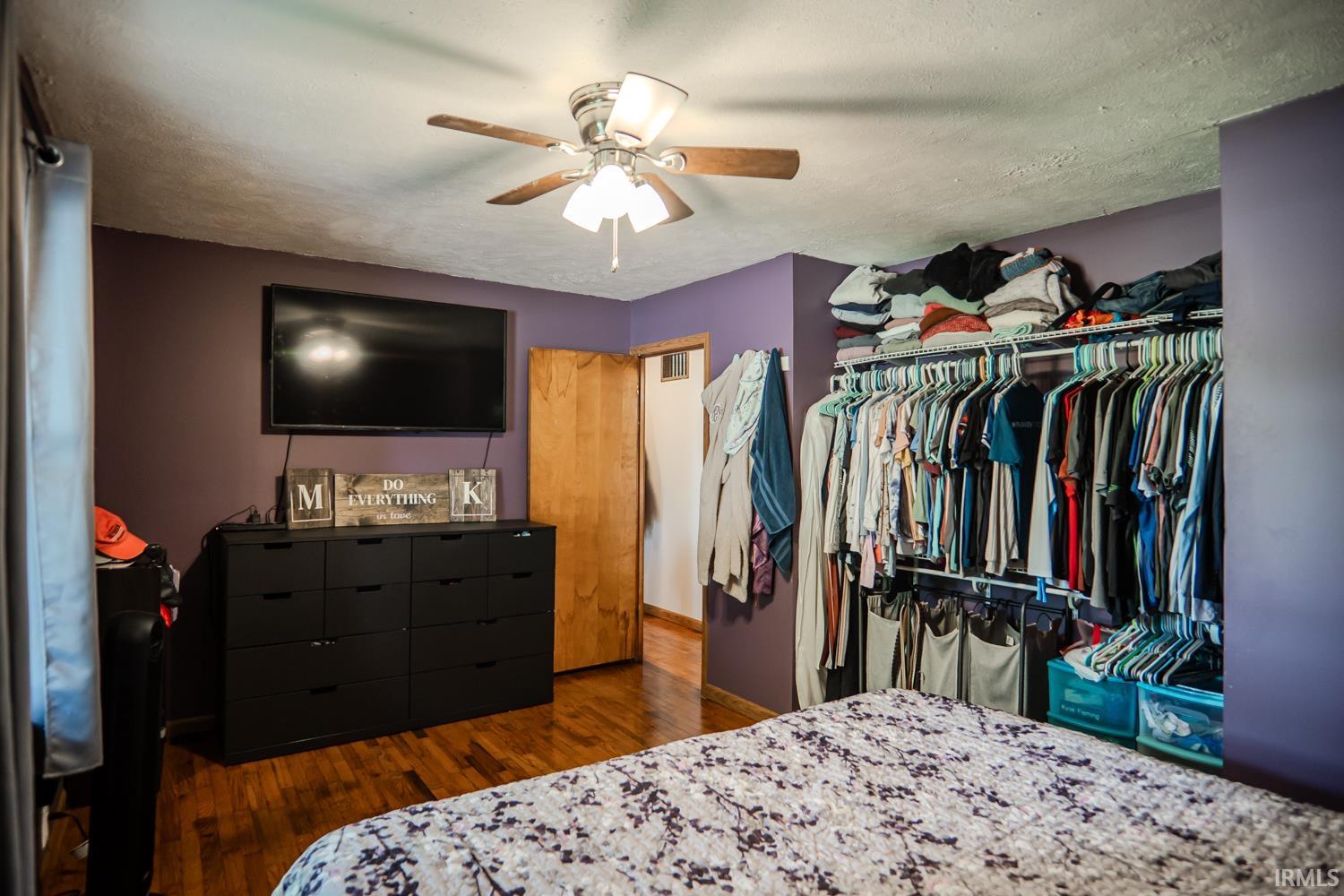 Bedroom featuring wood-finish flooring, a ceiling fan with integrated lighting, and a built-in closet system with shelving and hanging rods