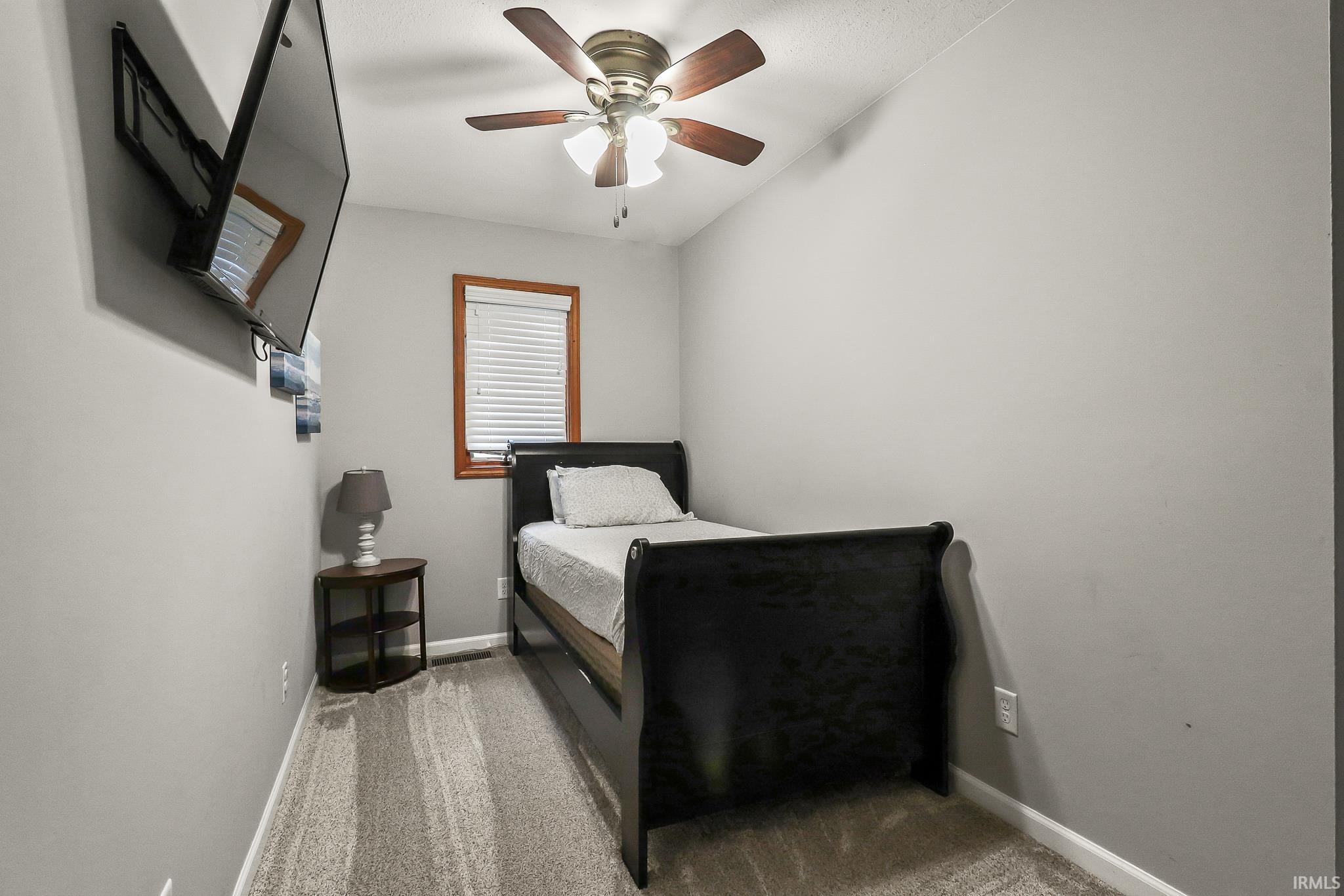 Room featuring wall-mounted television, ceiling fan with light fixture, window with blinds, and neutral-toned carpeting