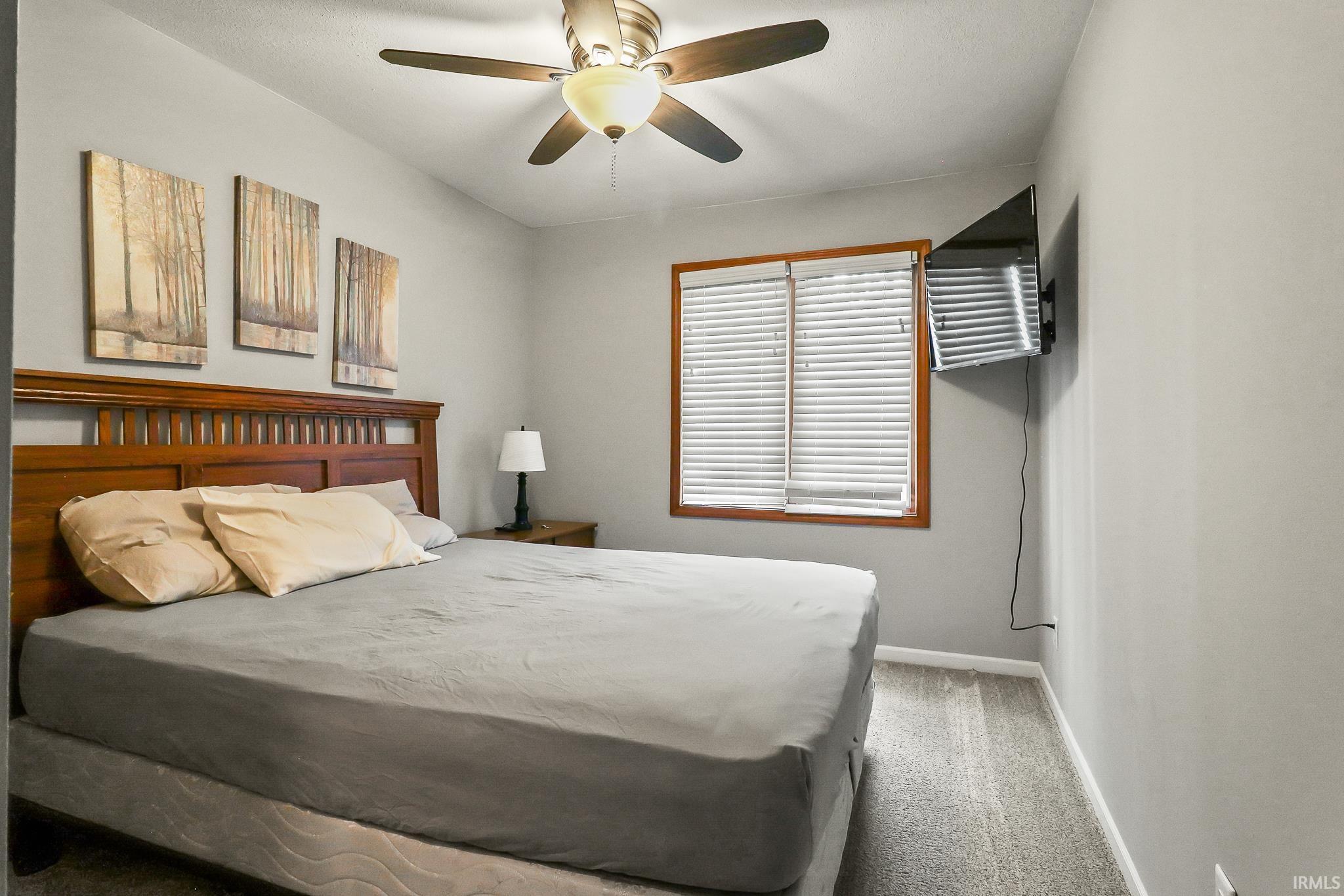 Carpeted room featuring a ceiling fan with light fixture, a window with wood trim and horizontal blinds, and neutral wall paint