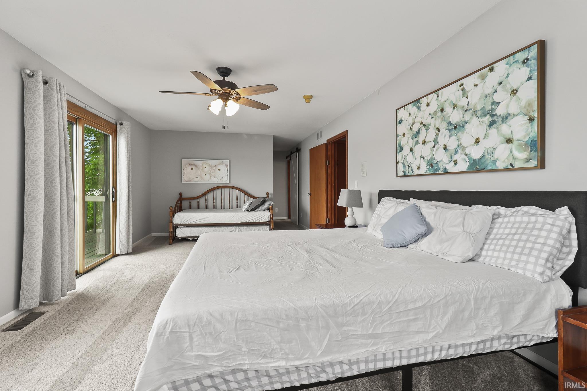 Spacious room featuring light gray carpeting, a ceiling fan with integrated lighting, and a sliding glass door providing exterior access