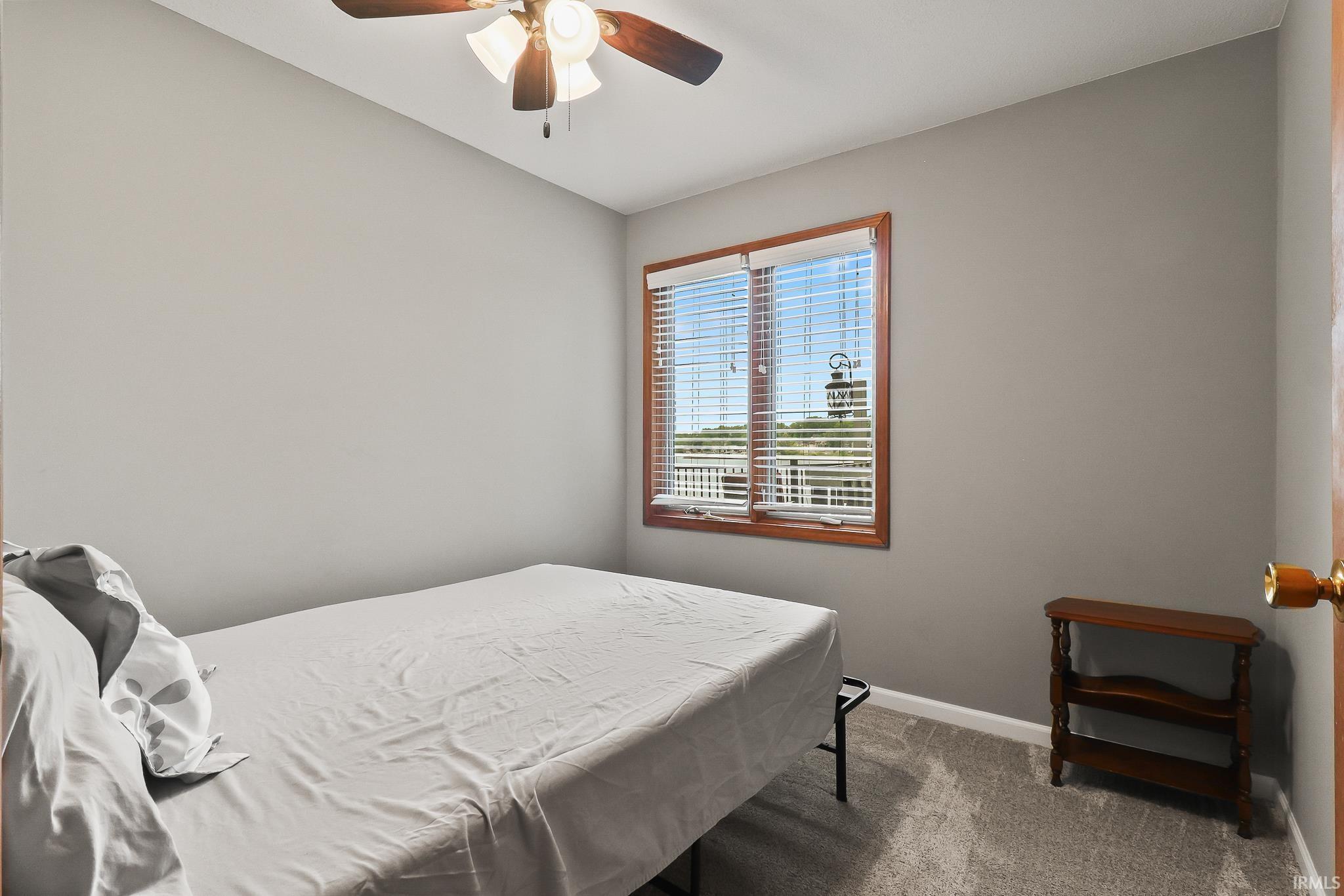 Bedroom featuring neutral gray walls, plush gray carpeting, and a window with wood-finish trim