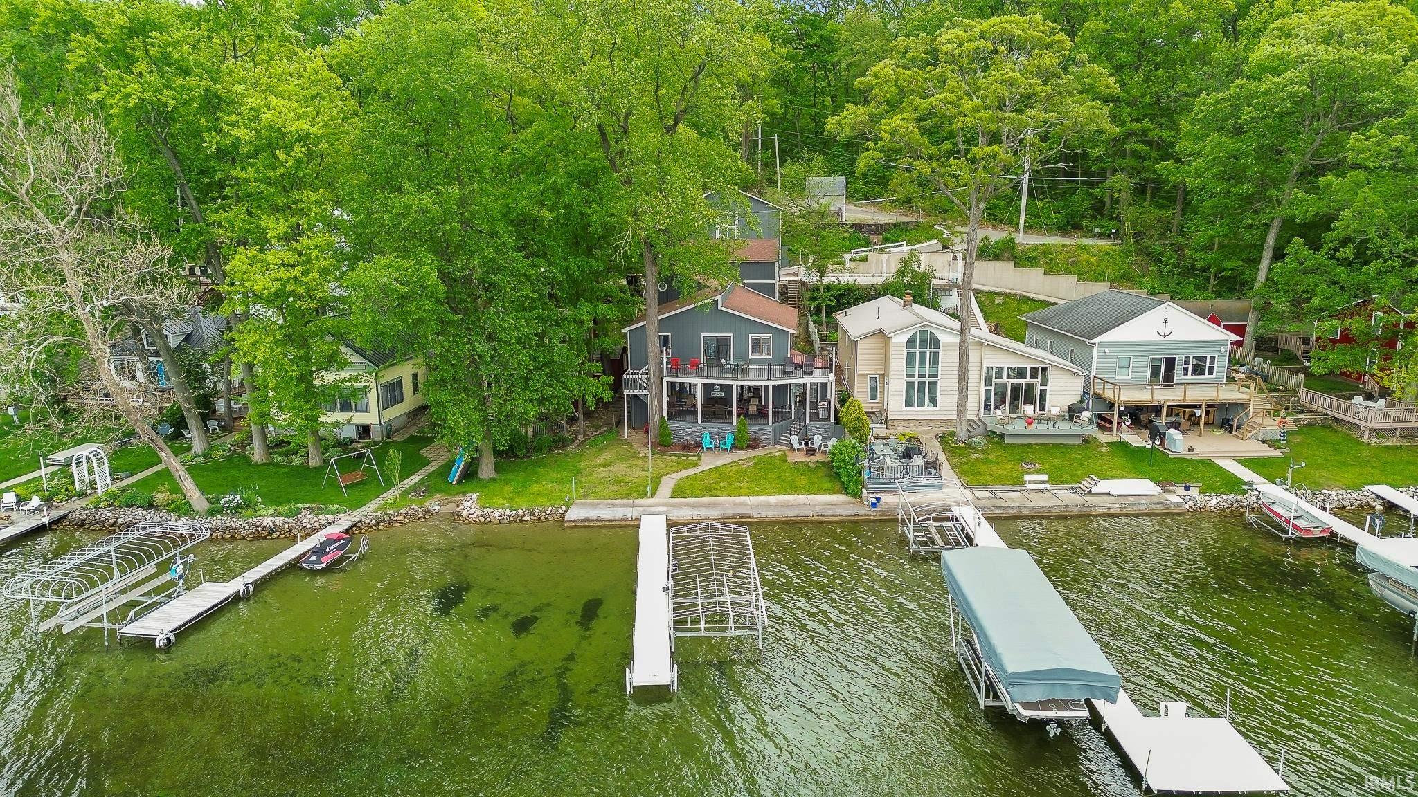 Waterfront property with multiple private docks, expansive green lawn, mature trees, and a multi-level deck for outdoor living