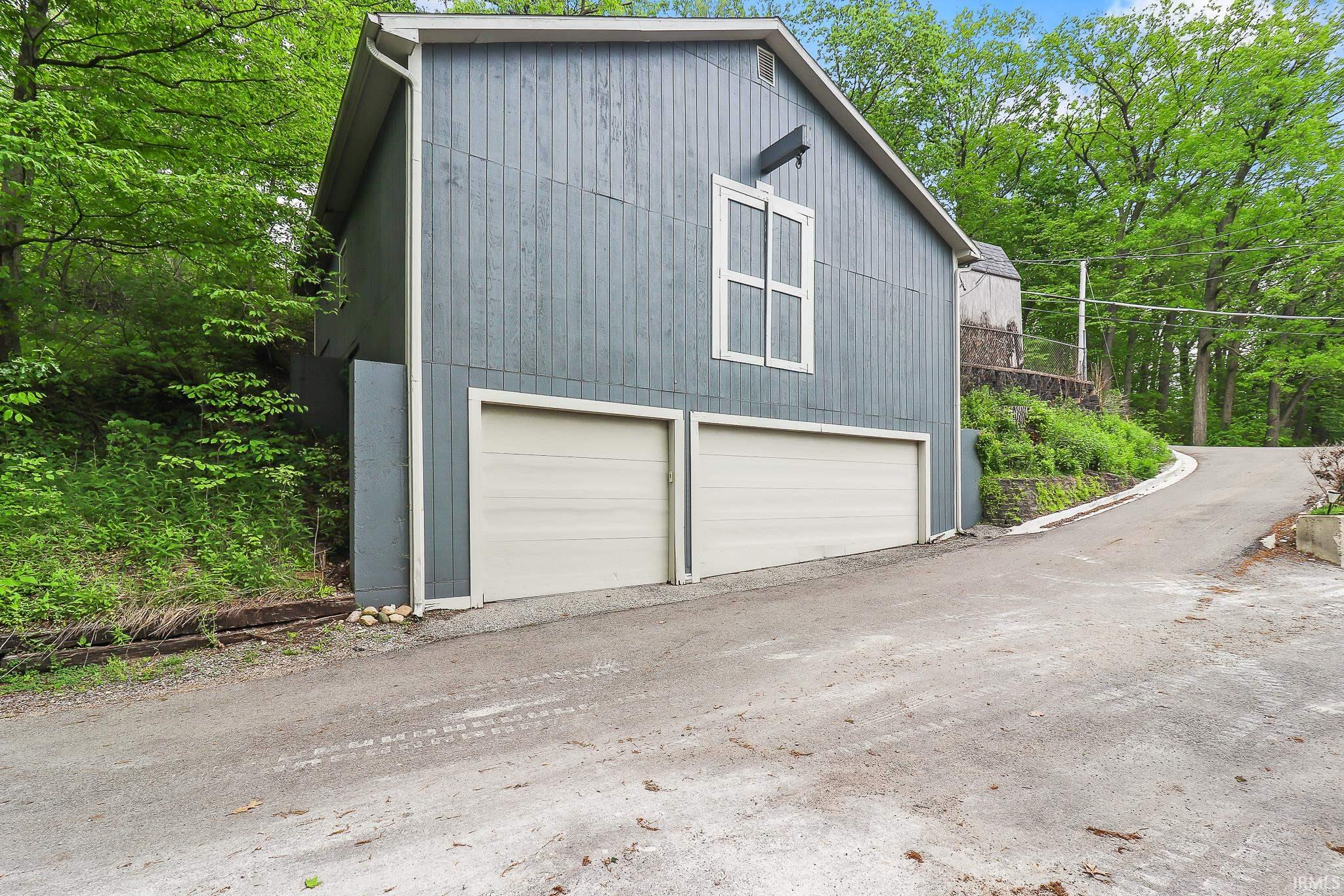 Exterior featuring a two-car garage with light-colored doors, a gray vertical siding facade, and white-framed windows