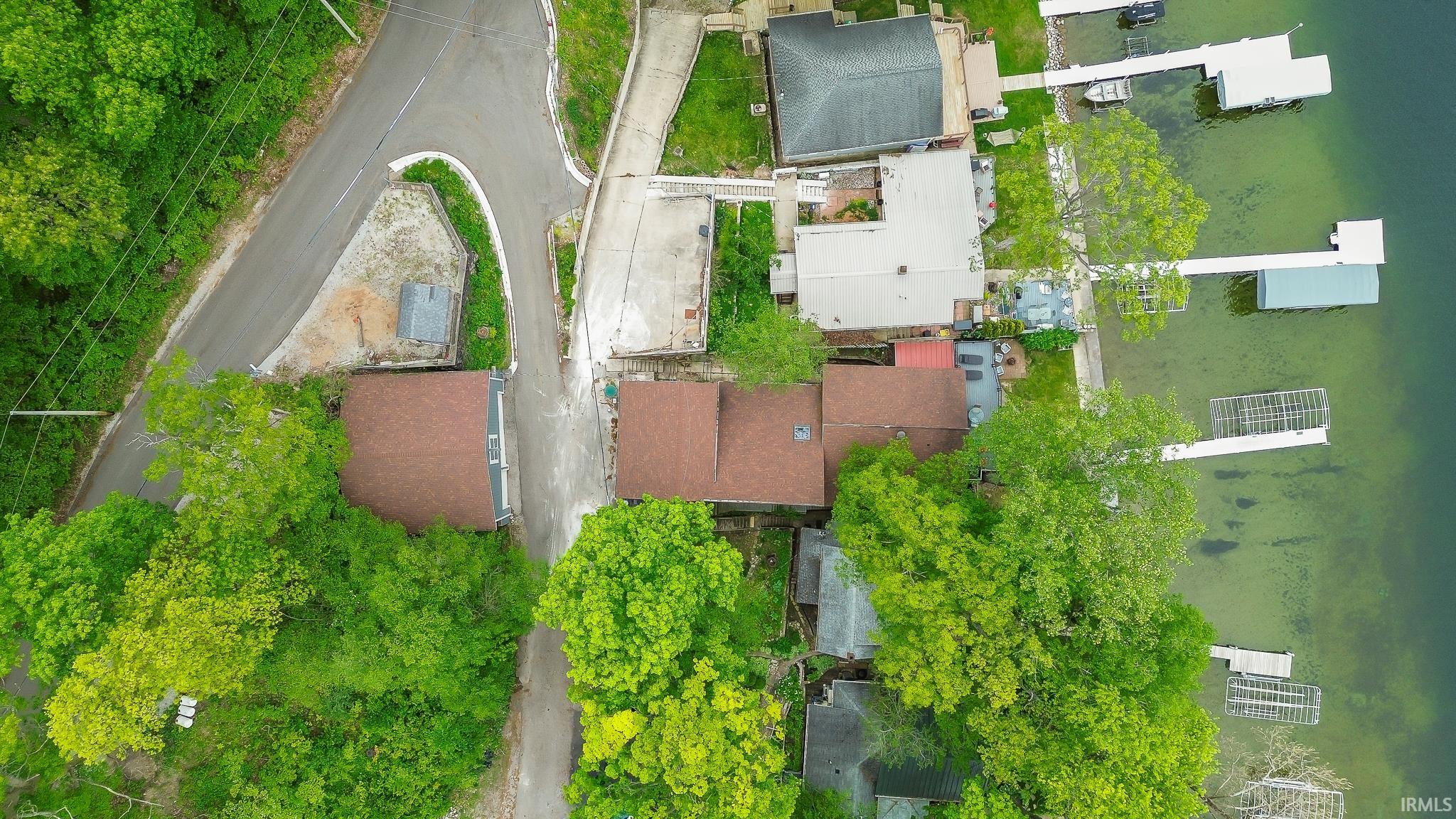 Aerial perspective showcasing a property with a brown shingle roof, surrounded by mature trees, and situated along a body of water