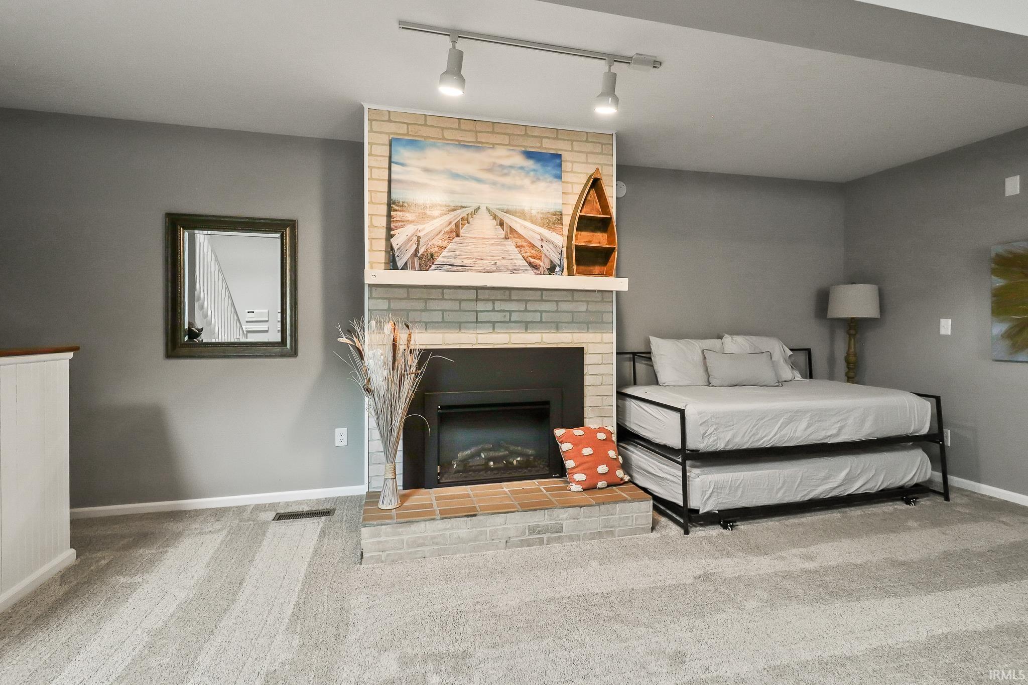 Carpeted living space featuring a brick-surround fireplace with a mantel, track lighting, and a neutral color palette