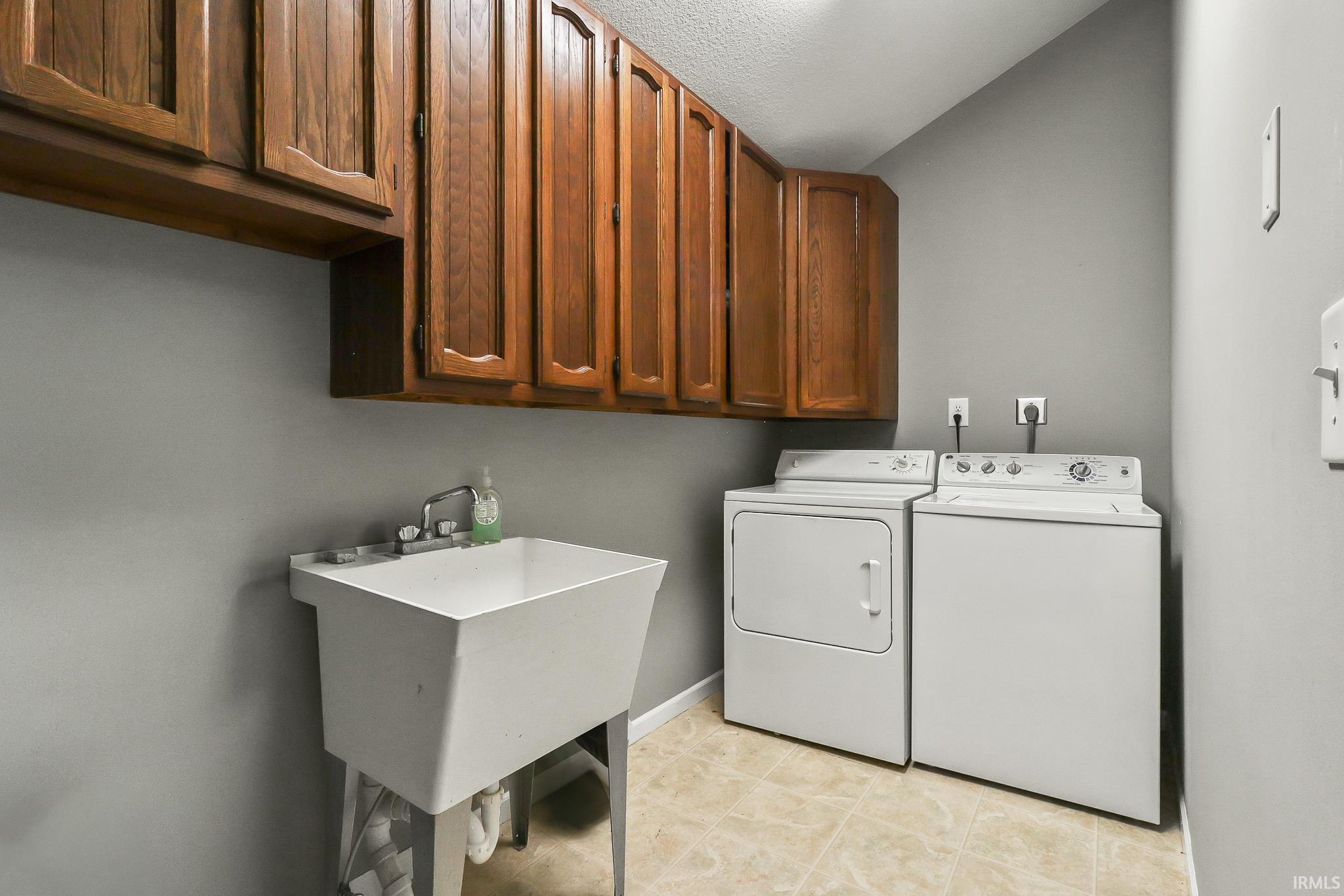 Utility room featuring wood-finish cabinetry, a large utility sink, and tile flooring