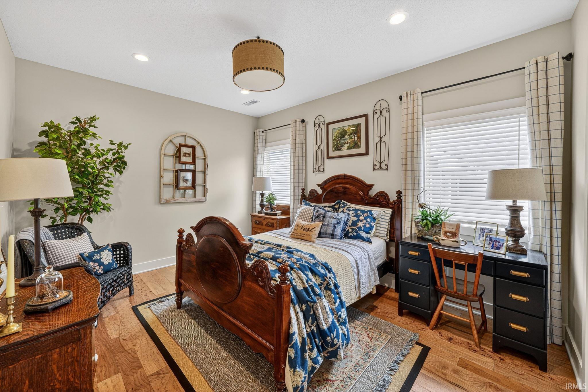 Bedroom featuring warm wood-finish flooring, recessed lighting, a central drum pendant light fixture, crisp white baseboards, and neutral wall tones