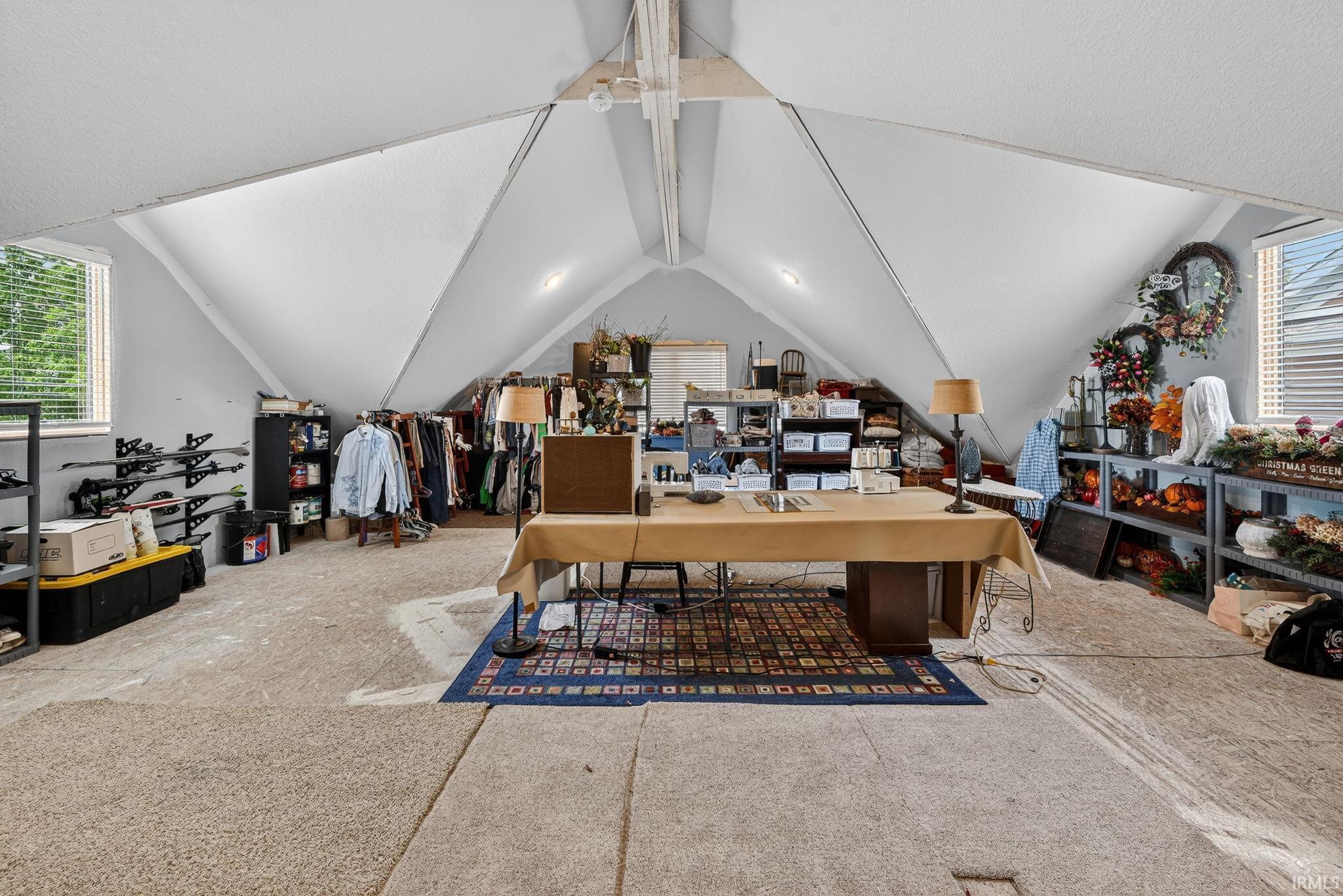 Spacious attic area featuring sloped ceilings, two rectangular windows with blinds, and light-colored carpeting