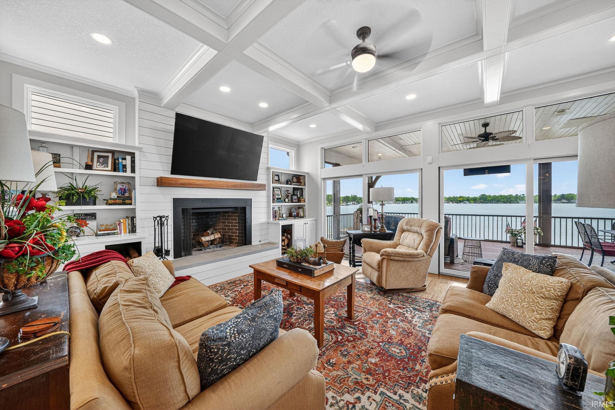 Spacious living area featuring a coffered ceiling, shiplap-accented walls, a fireplace with a stone hearth, and built-in shelving