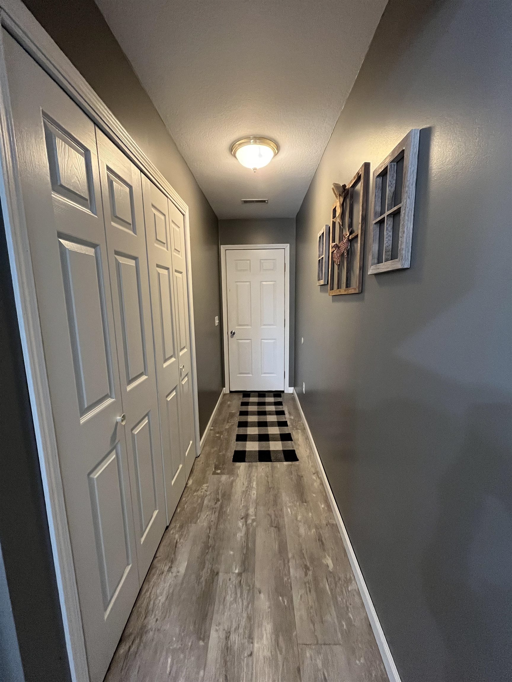 Hallway with wood-finish flooring, neutral gray walls, and white bi-fold closet doors