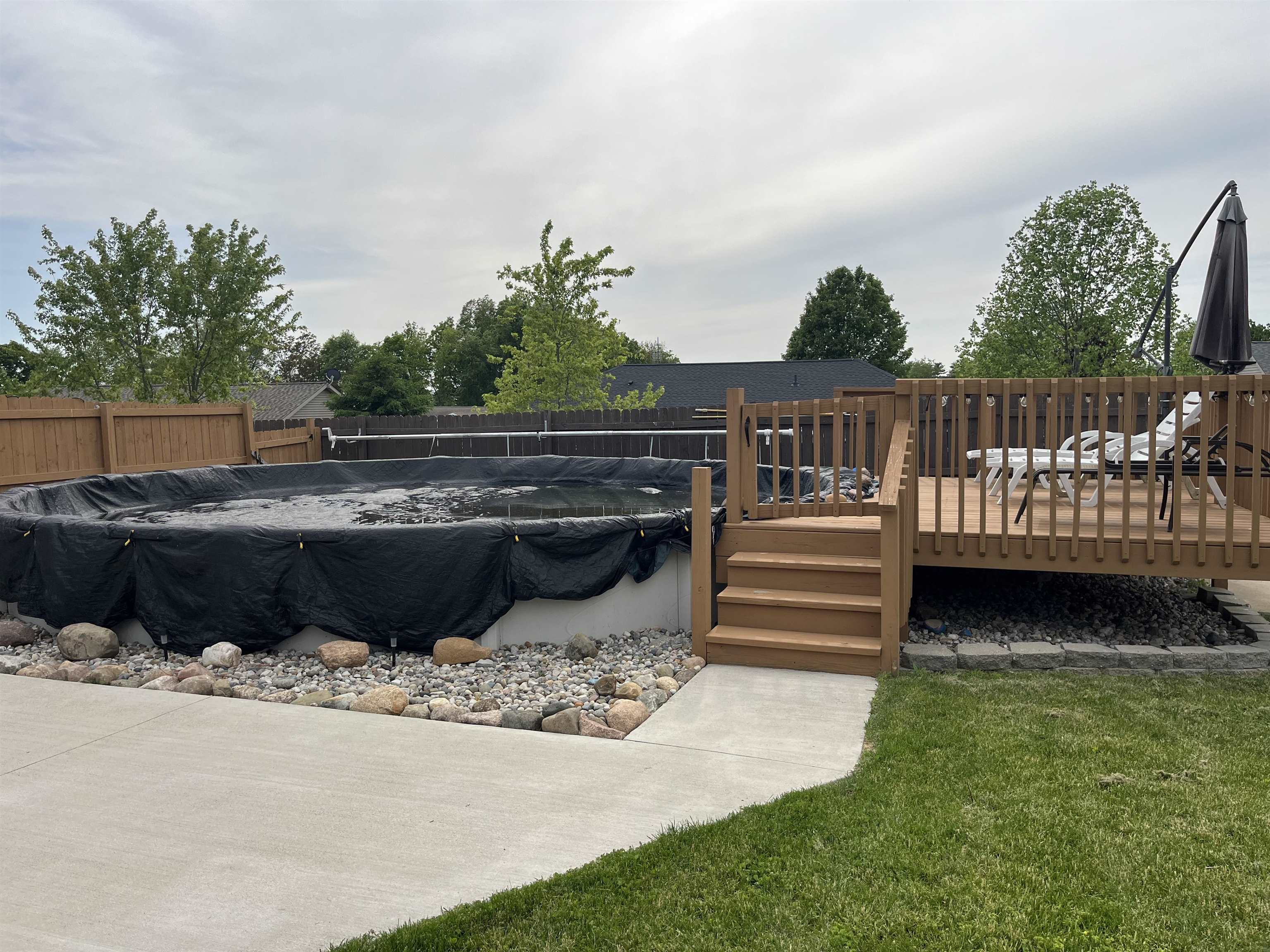 Backyard area featuring an above-ground pool, expansive wood deck with railing, concrete patio, and a privacy fence