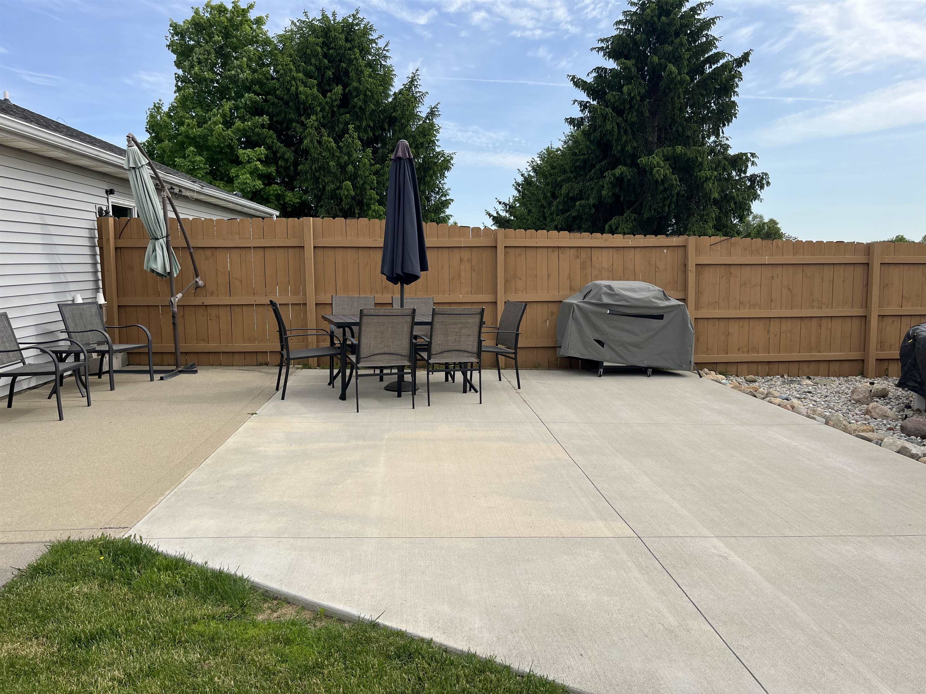 Spacious concrete patio featuring a wood privacy fence and decorative rock landscaping