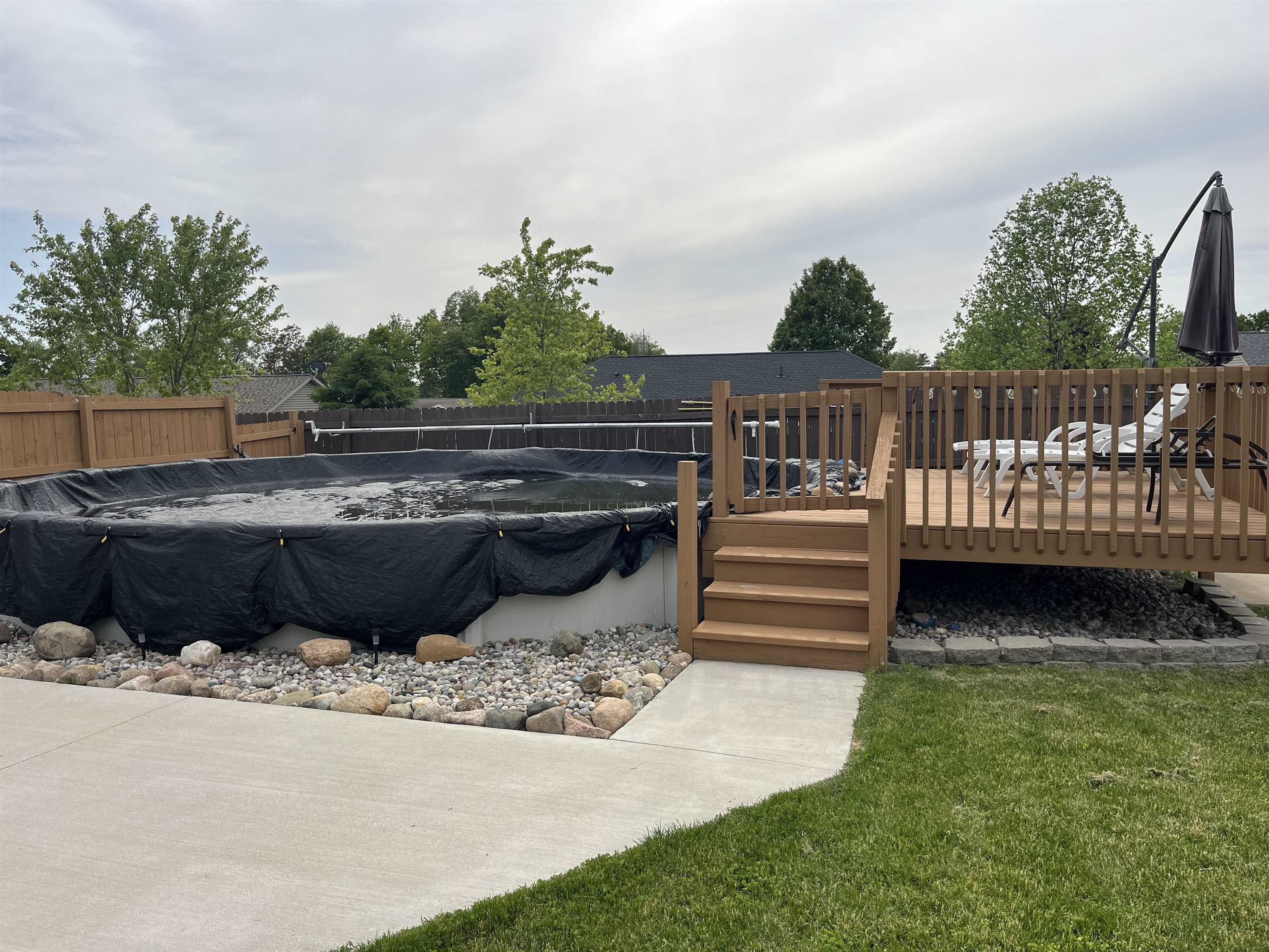 Expansive backyard featuring an above-ground pool, a wooden deck with railing, concrete patio, and a privacy fence