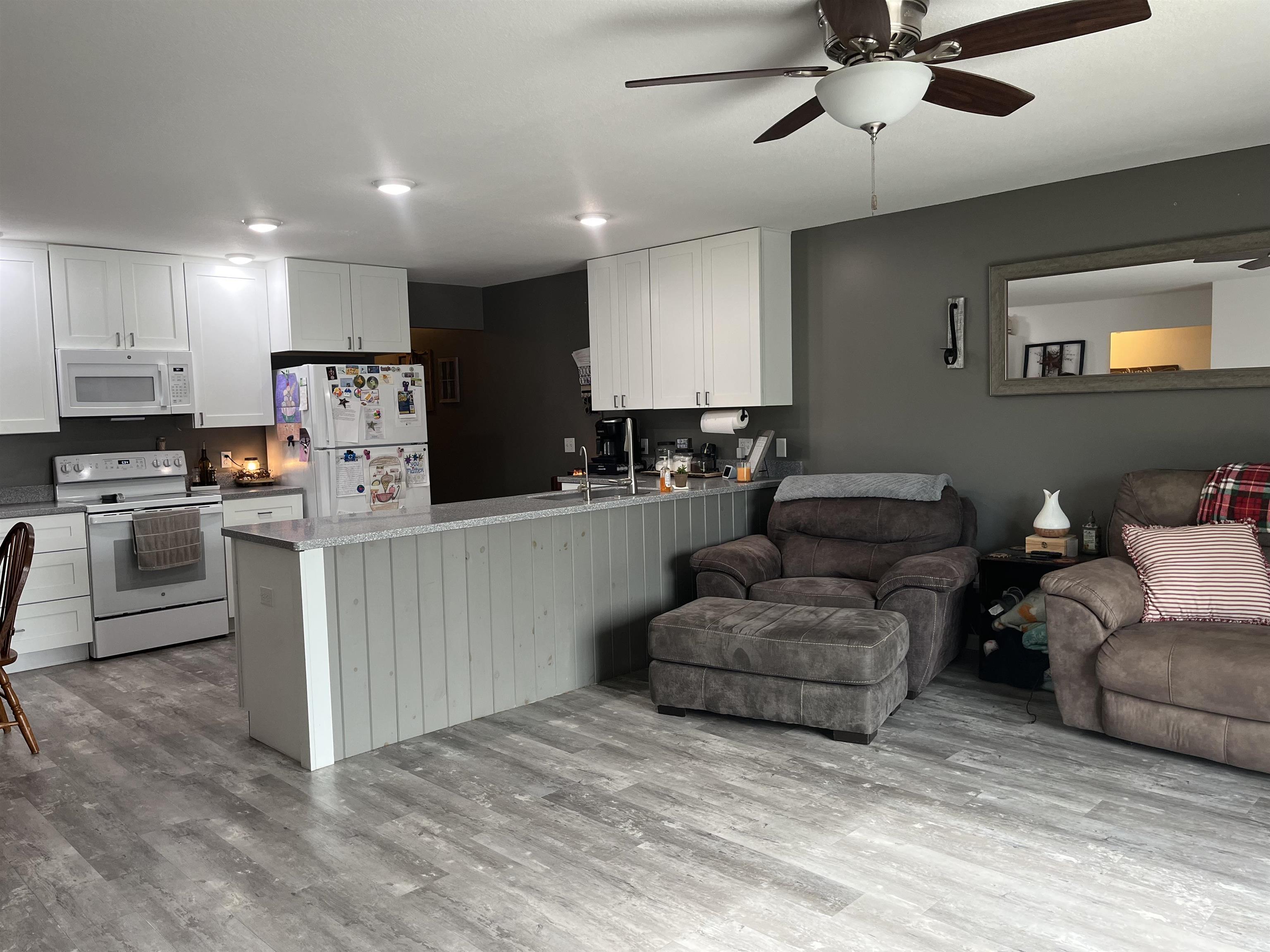 Open-concept living space featuring a kitchen with white cabinetry and white appliances, a peninsula with a beadboard-style base, and wood-finish flooring throughout