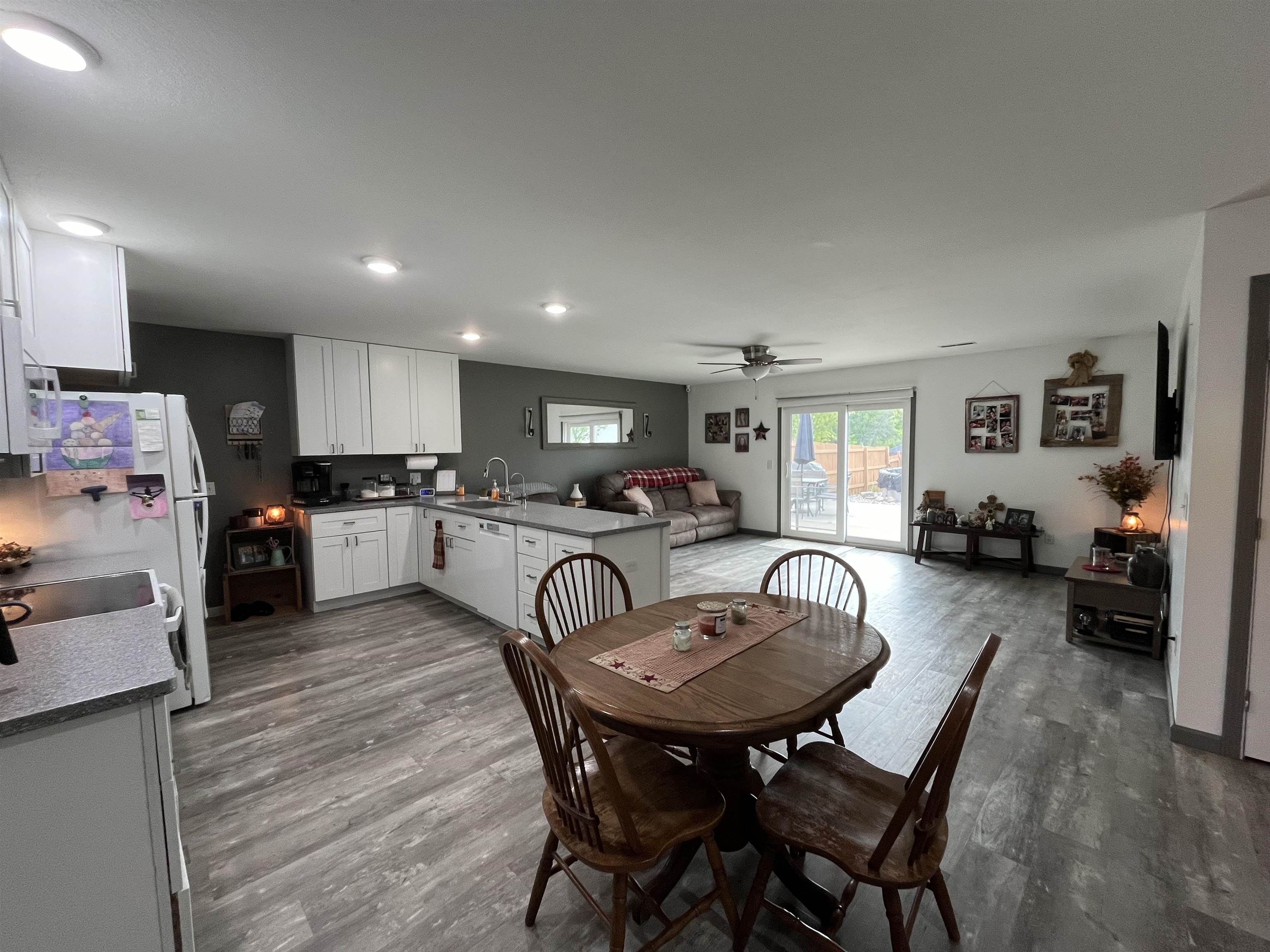 Open-concept living space featuring wood-finish flooring throughout, a kitchen with white cabinetry and light-toned countertops, and a living area with a ceiling fan