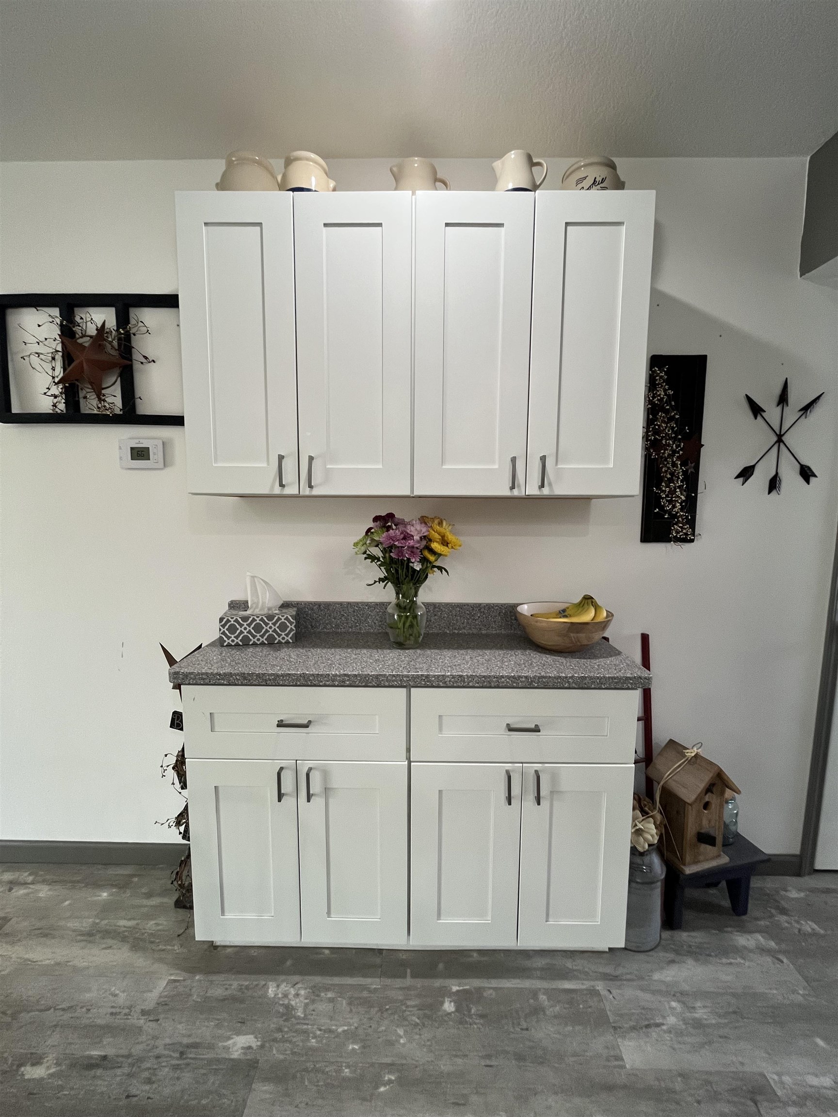 White shaker-style cabinetry featuring upper and lower storage, complemented by a speckled countertop and wood-finish flooring