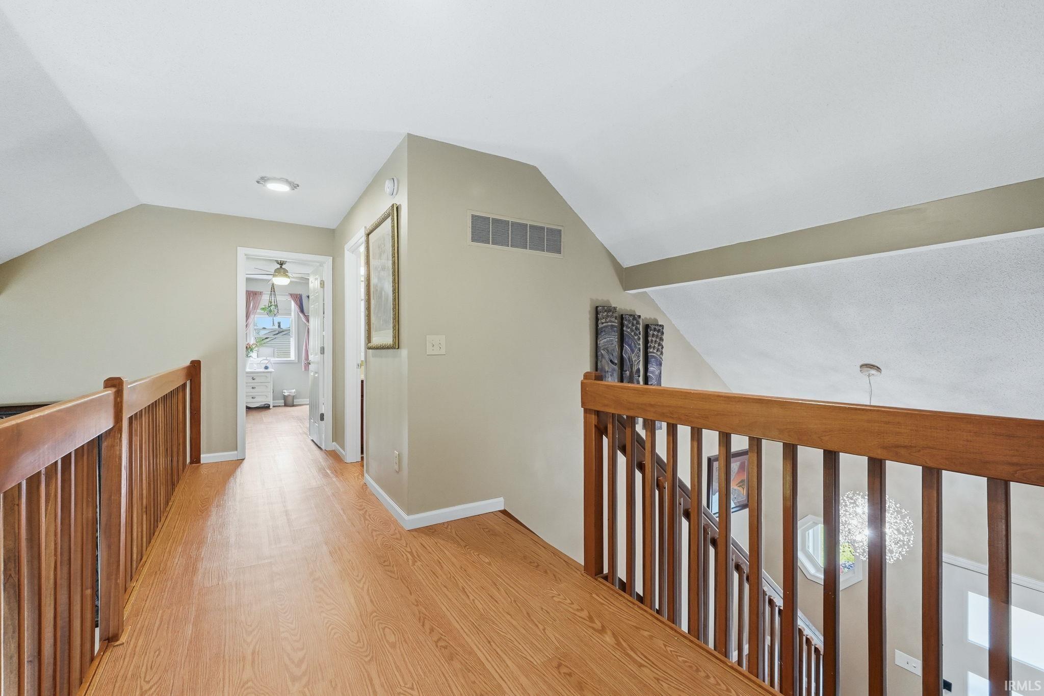 Upper-level hallway featuring wood-finish flooring, light-toned wall paint, and a wood railing overlooking the lower level