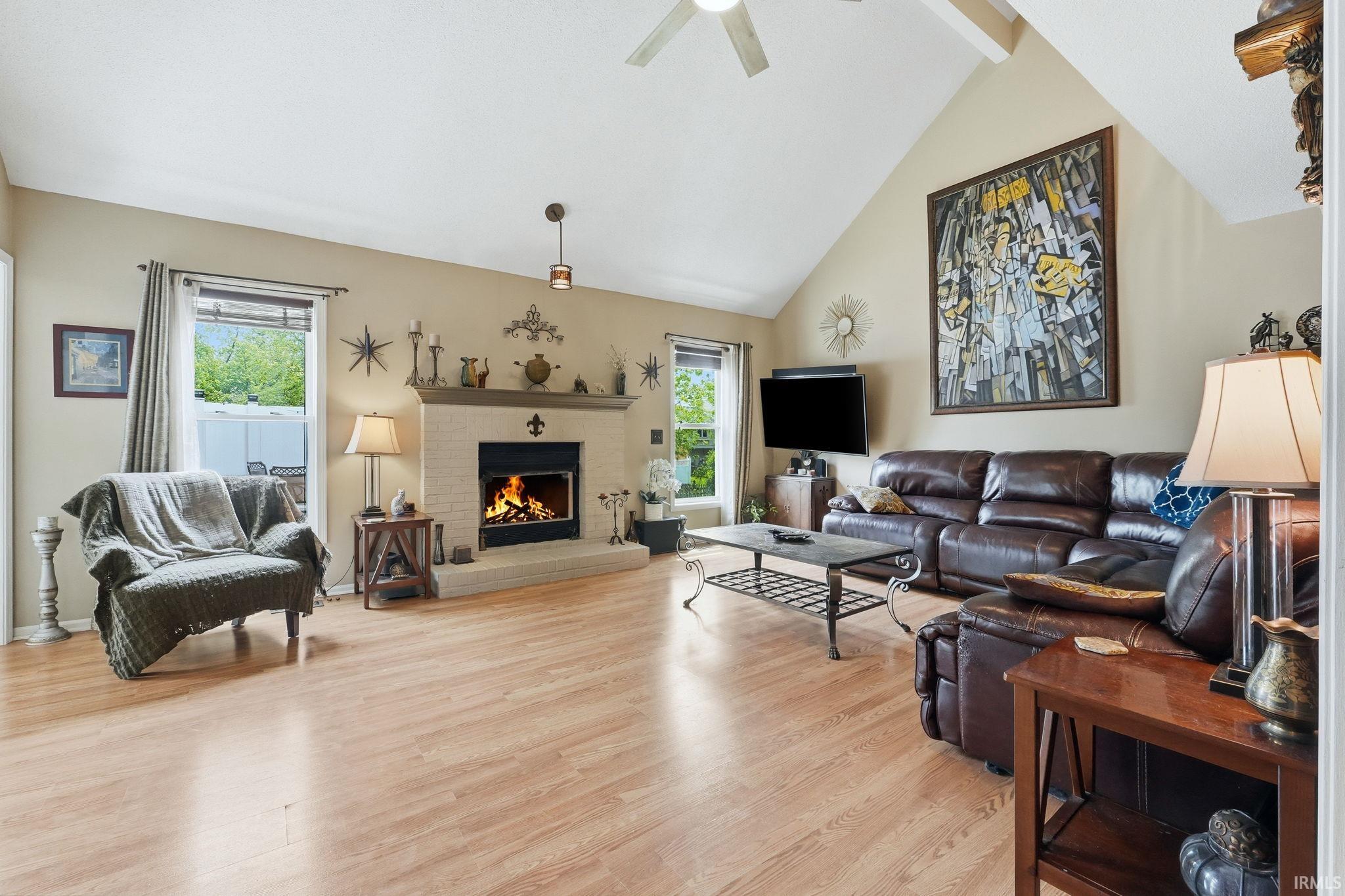 Vaulted ceiling with exposed beam detailing, wood-finish flooring, and a brick-surround gas-log fireplace with a mantel