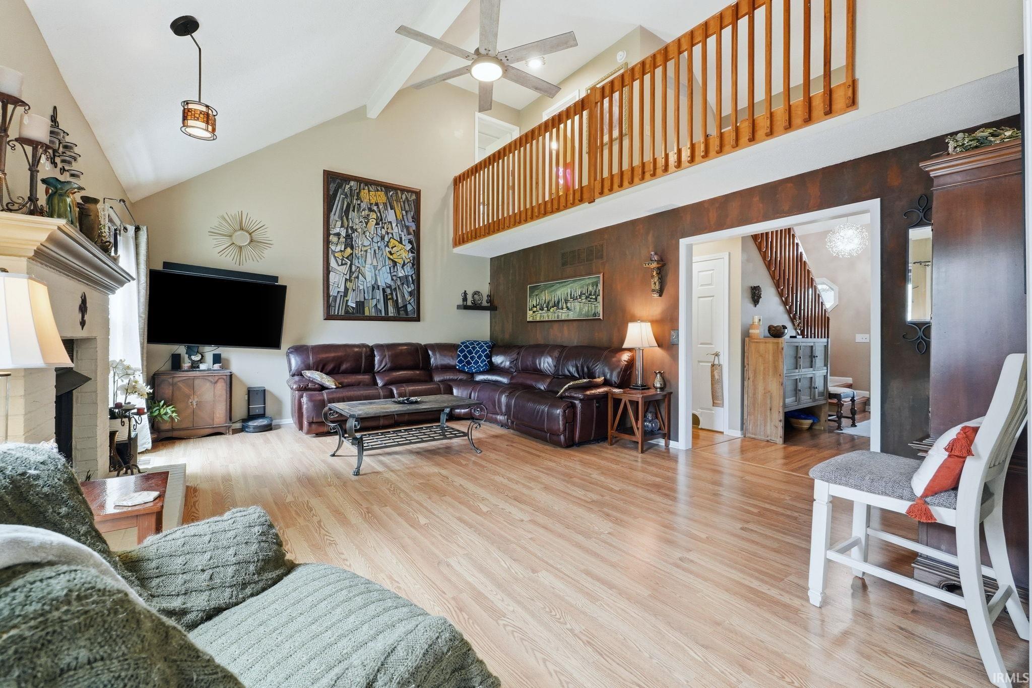 Vaulted ceiling with an overhead fan and recessed lighting, light wood-finish flooring, and an upper-level balcony with wood railings