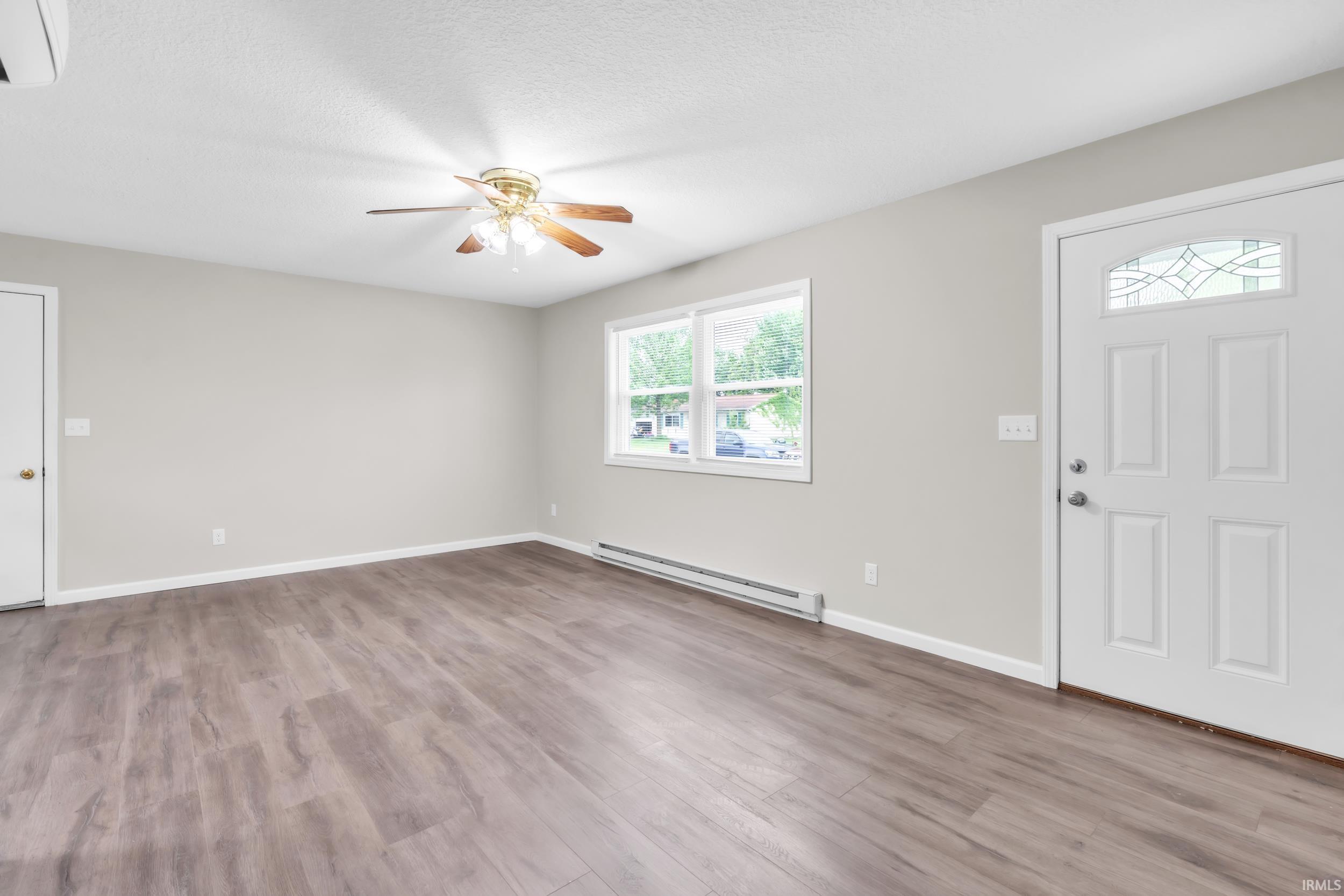 Spacious living area featuring wood-finish flooring, light gray walls, a ceiling fan, and a white entry door with decorative glass inserts