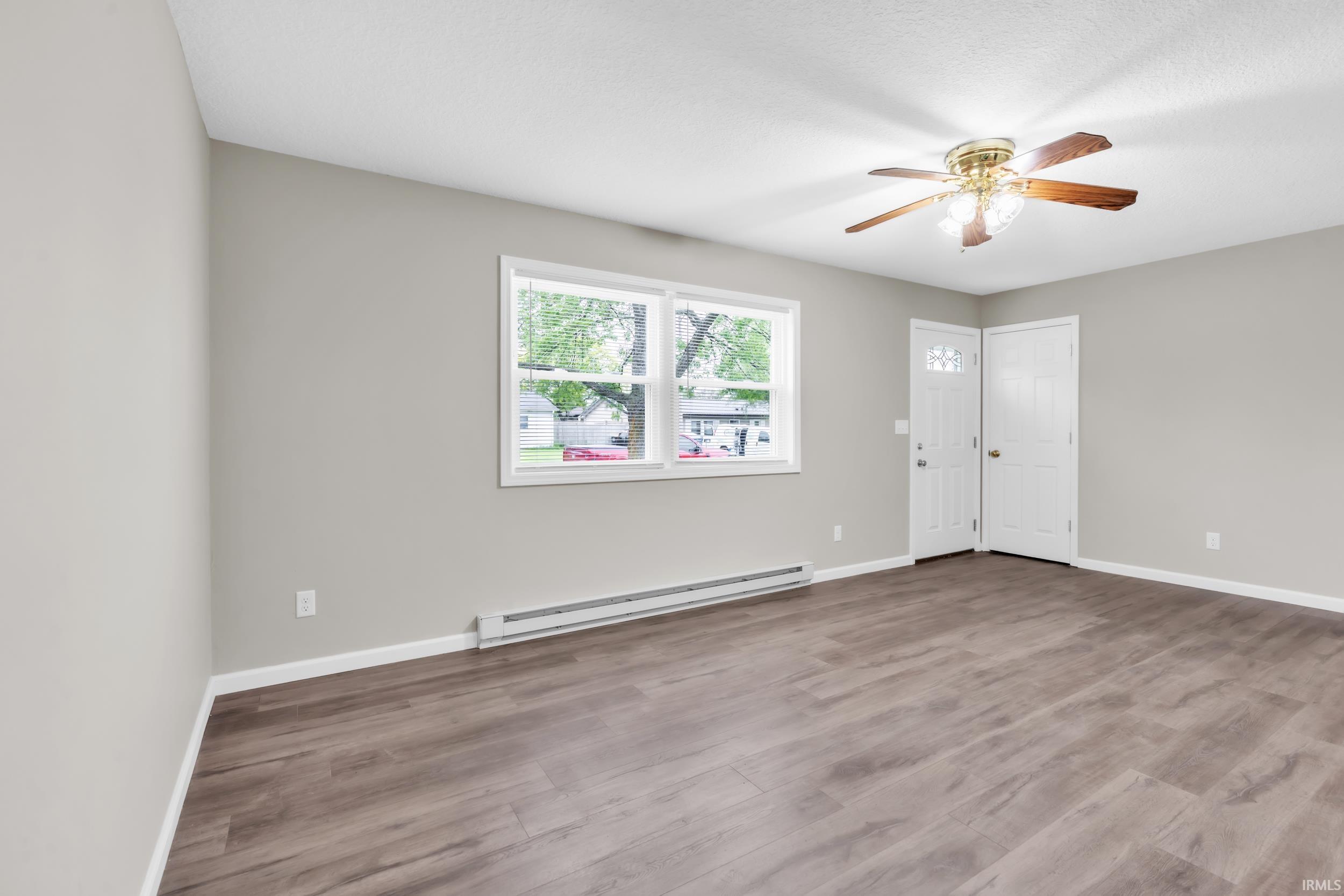 Spacious room featuring wood-finish flooring, light grey walls, and a multi-pane window