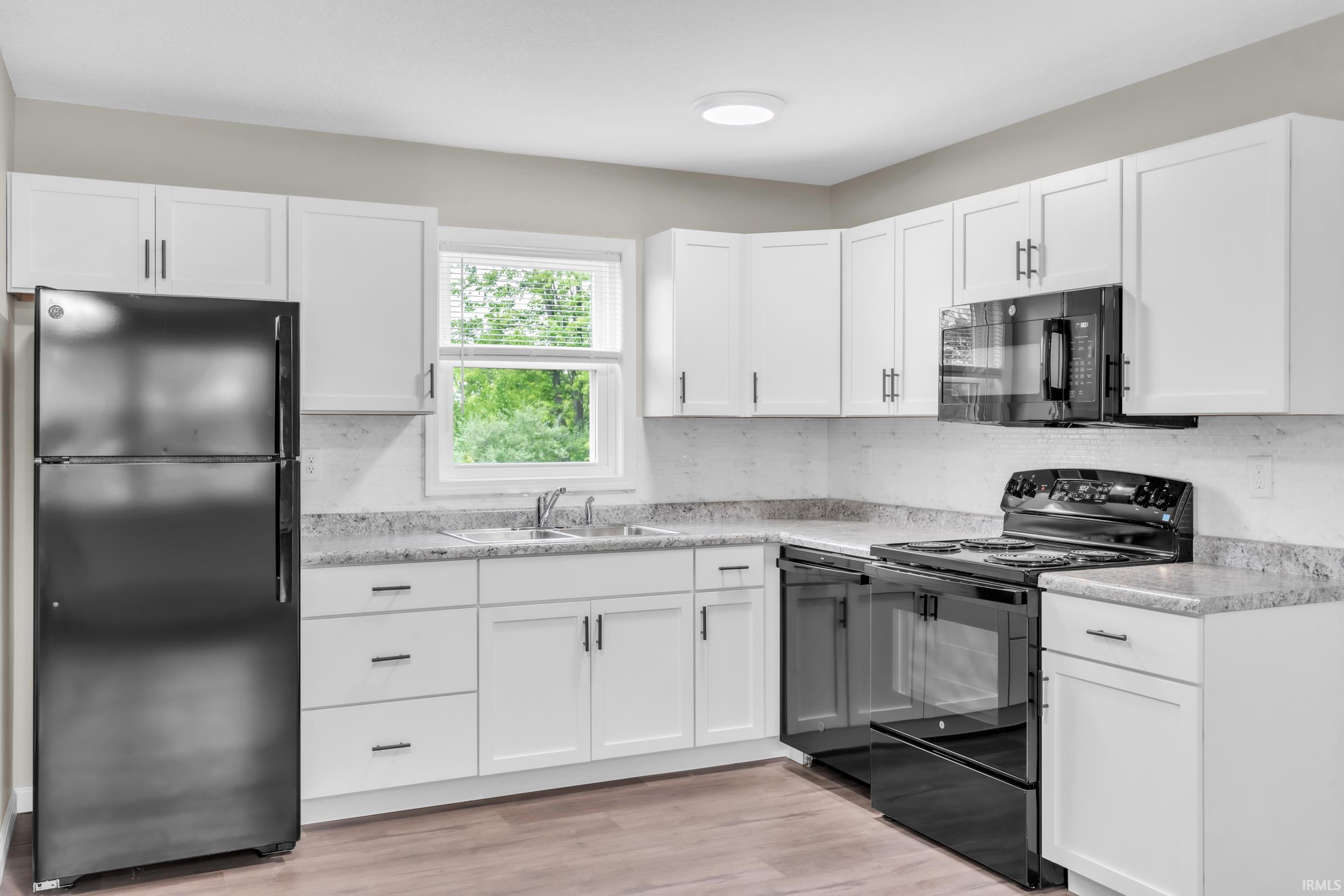 Modern kitchen featuring white cabinetry with dark hardware, granite-look countertops, and a full suite of black appliances