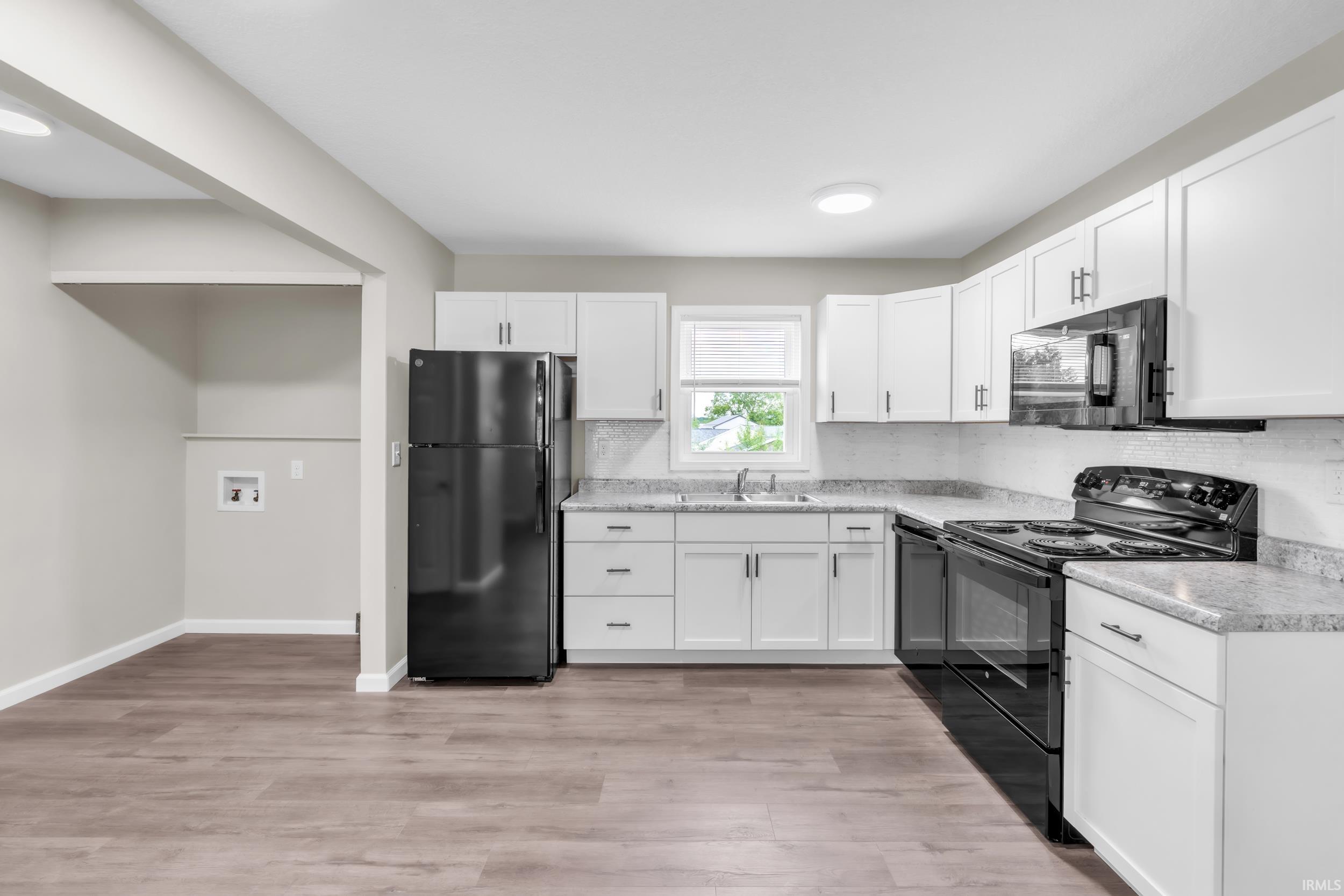 Kitchen featuring white cabinetry, light-toned countertops, a full suite of black appliances, and wood-finish flooring