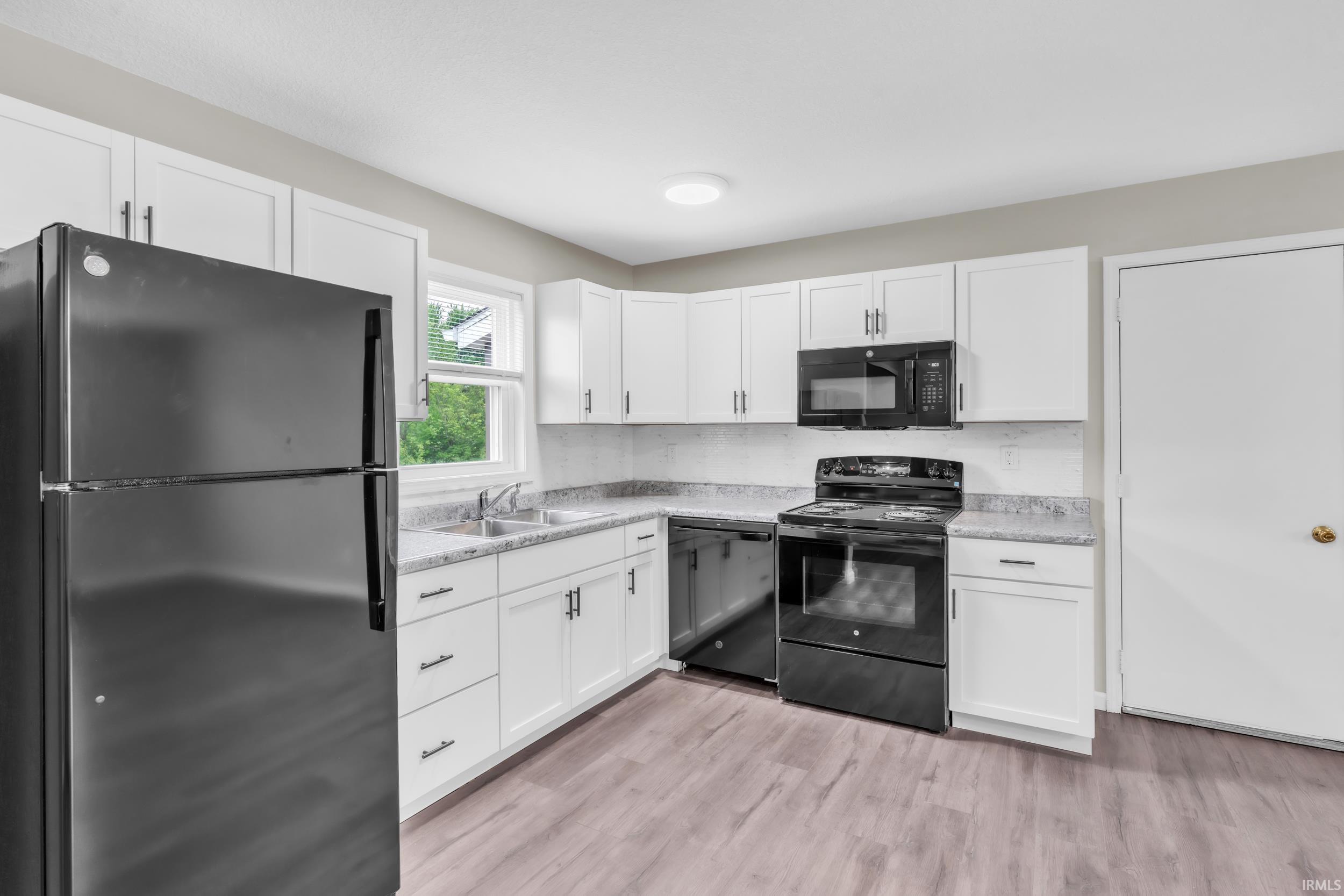 Kitchen featuring white cabinetry, wood-finish flooring, a double basin sink, black appliances, and a window above the sink