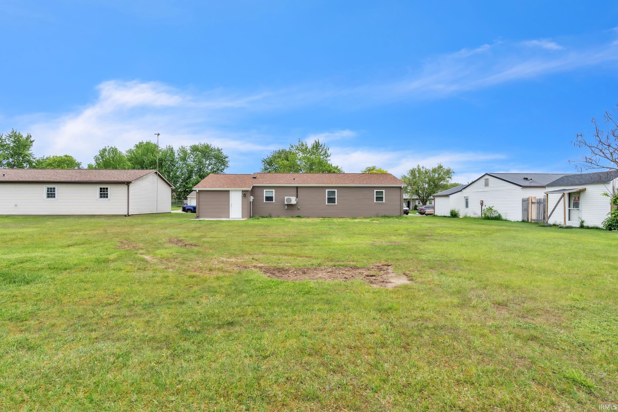 Expansive grassy yard area with a brown-sided structure featuring multiple windows and an air conditioning unit
